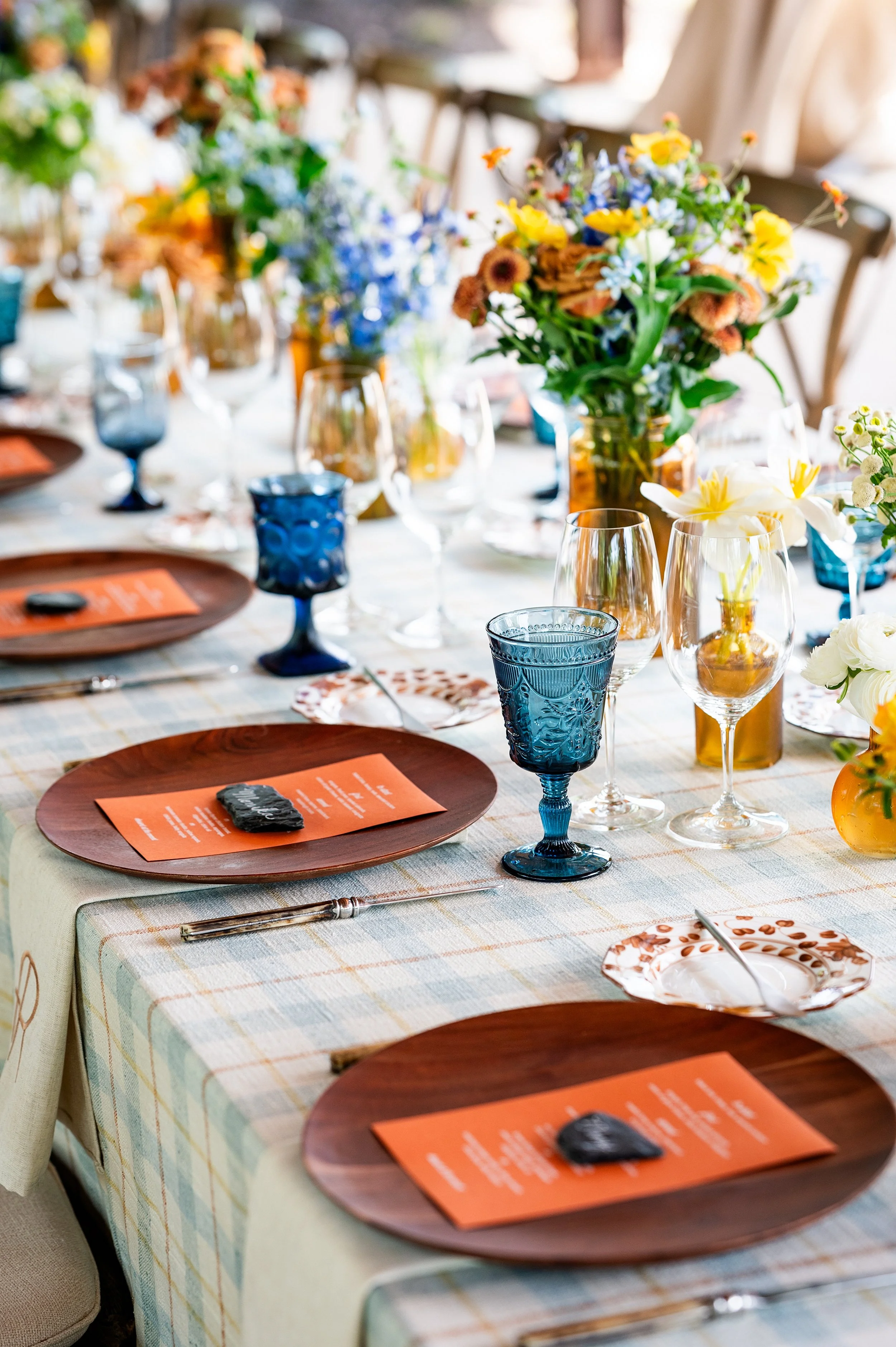 A table set for a meal with plates, glasses, and floral centerpieces in a bright, airy room.