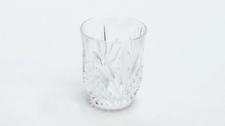 Empty cut glass tumbler with etched pattern on a white background