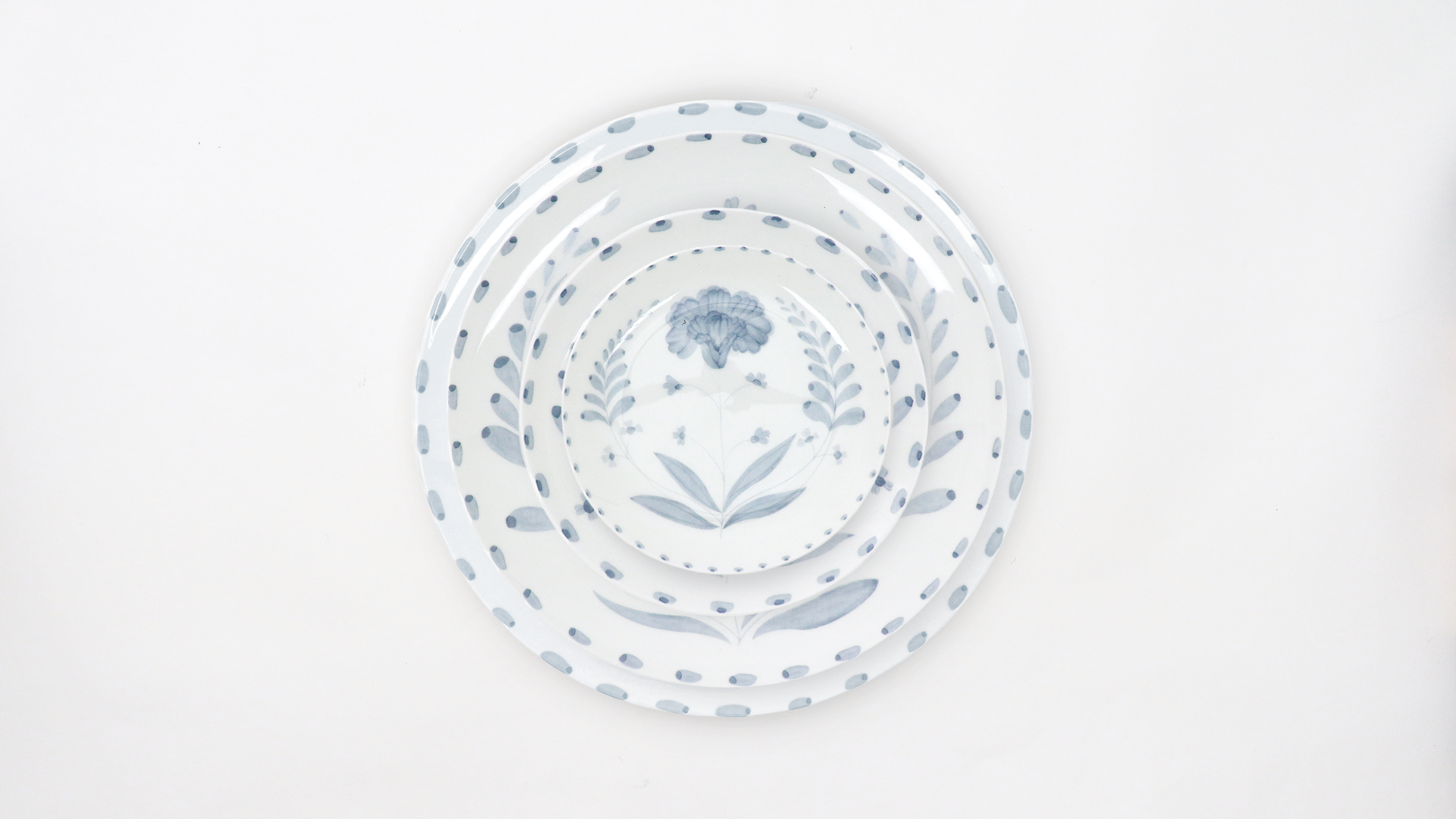 Three nested white plates with blue floral and dot patterns, arranged in a descending order on a white background.
