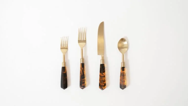 Set of four gold-colored utensils with tortoise shell handles: two forks, one knife, and one spoon, arranged on a white background.