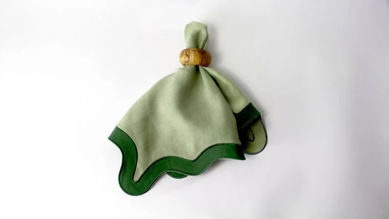 A cloth napkin tied with a cork, with the napkin having a green border, hanging on a white background.
