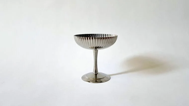 A shiny silver dessert cup with a fluted design on a plain white background.