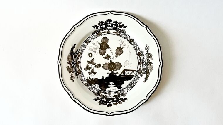 Decorative ceramic plate with black and white floral and landscape pattern hanging on a wall