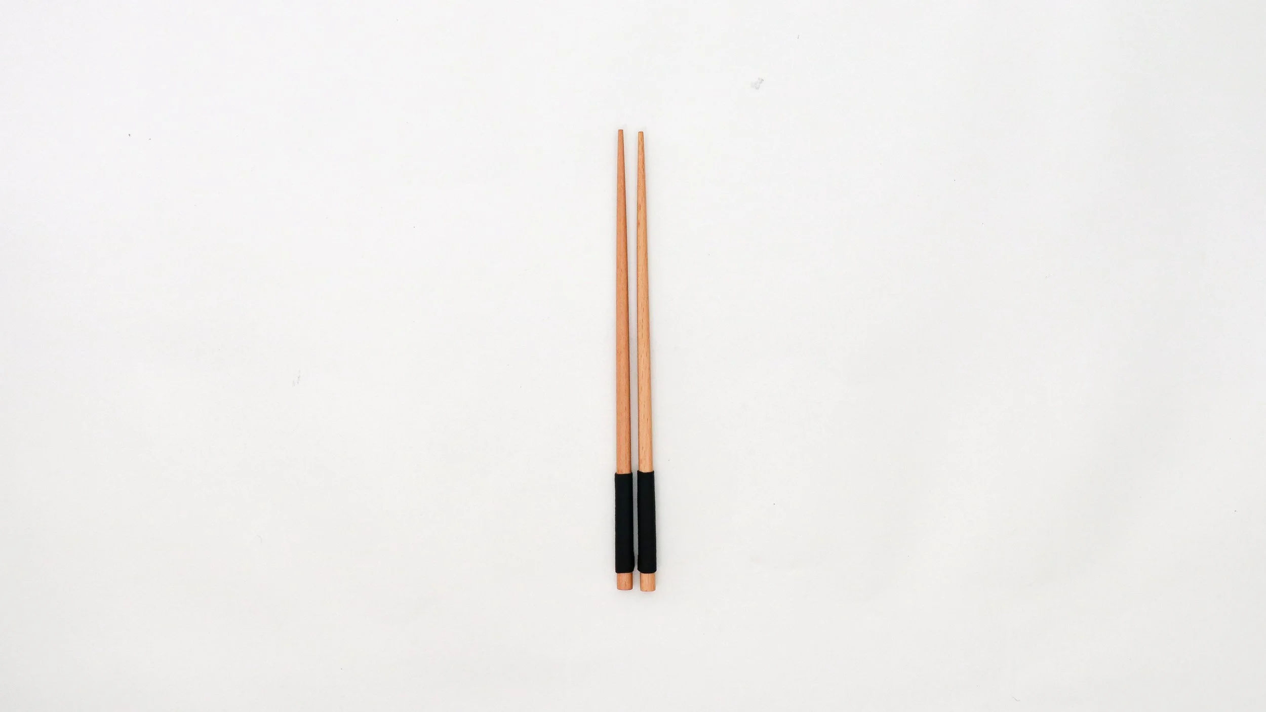 A pair of wooden chopsticks with black handles lying parallel on a white surface.