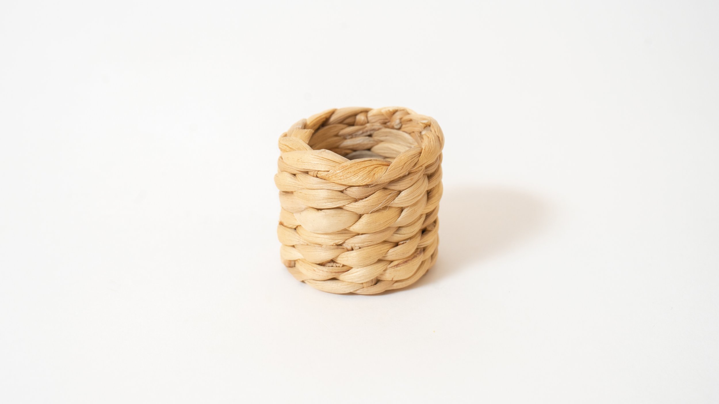A small wicker woven basket with a round shape placed on a white surface with a plain white background.