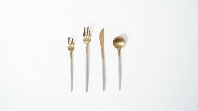 A set of four gold and white utensils, including a fork, knife, and spoon, arranged on a white background.