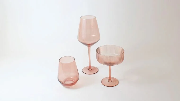 Three pink glassware pieces: a tall wine glass, a short tumbler, and a wide-rimmed cocktail glass, all on a white surface.