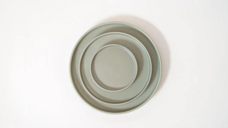 A set of three nested ceramic bowls in taupe color on a white background.