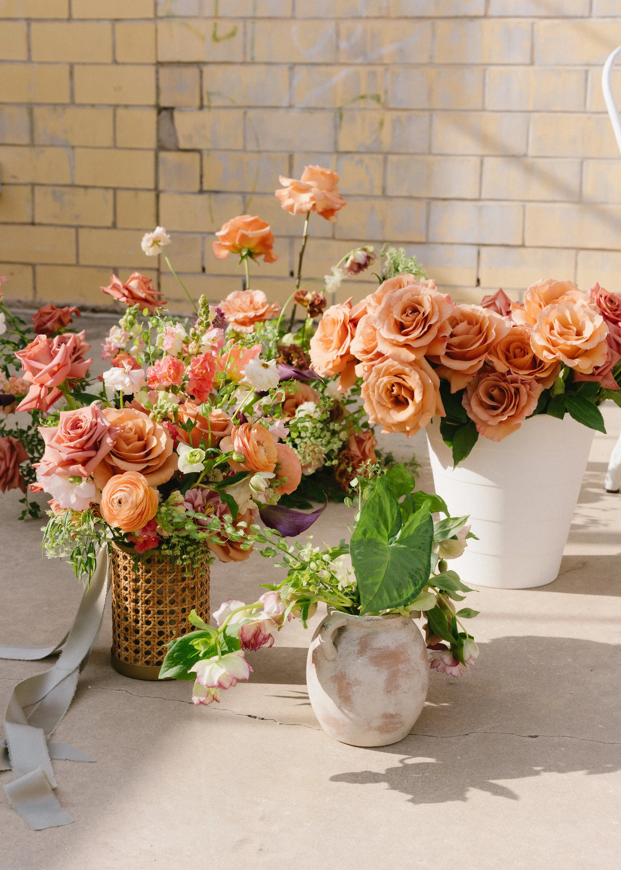 Arranged peach and pink flowers in vases on a concrete surface with a brick wall background.