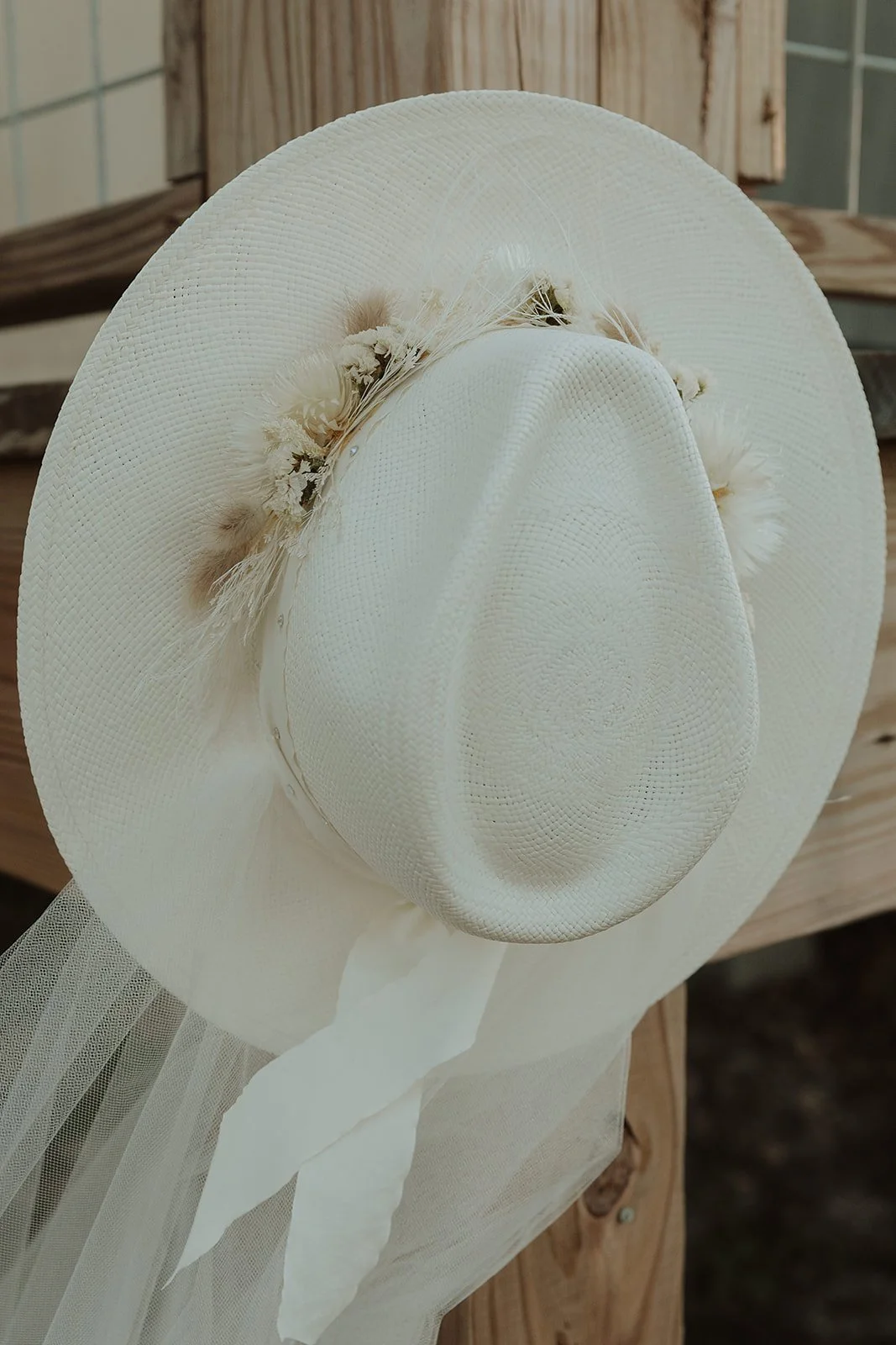Straw sun hat with a wide brim, decorated with dried flowers and feathers, resting on a wooden surface.