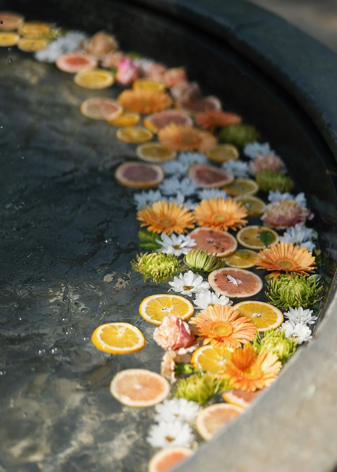 Floating citrus slices and colorful flowers in water.