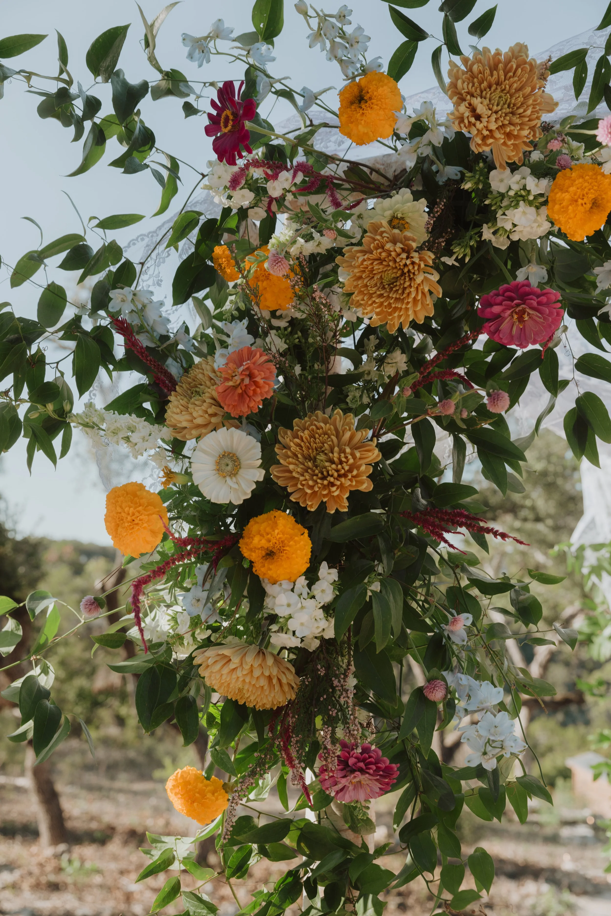 A floral arrangement with various colorful flowers and green leaves hanging outdoors.