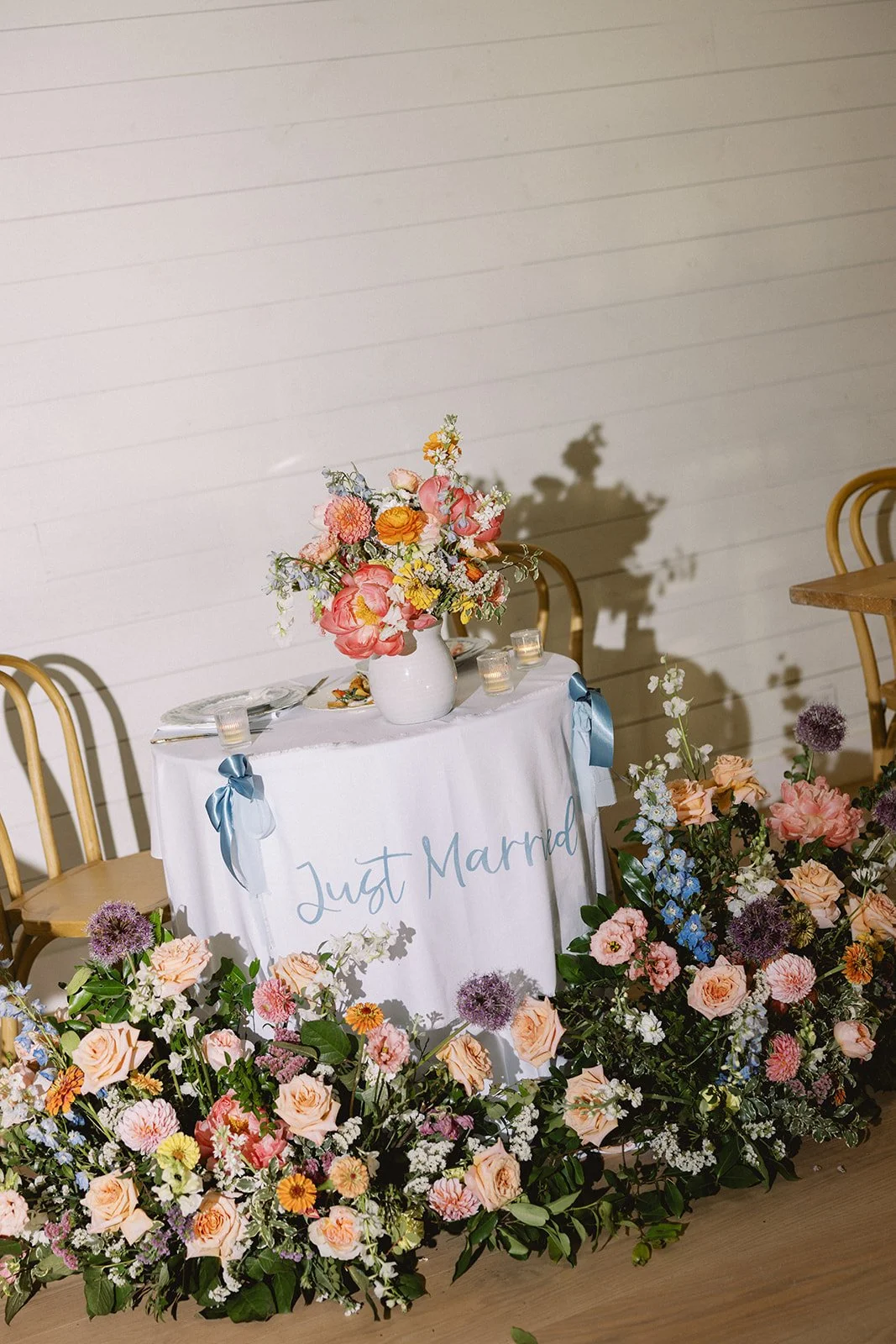 Wedding dessert table with a "Just Married" cake sign, surrounded by colorful flowers and a bouquet in a white vase.