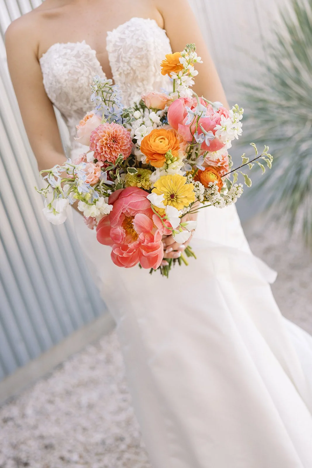 A bride holding a large bouquet of colorful flowers including pink, yellow, orange, and white blossoms, with her white wedding dress visible.