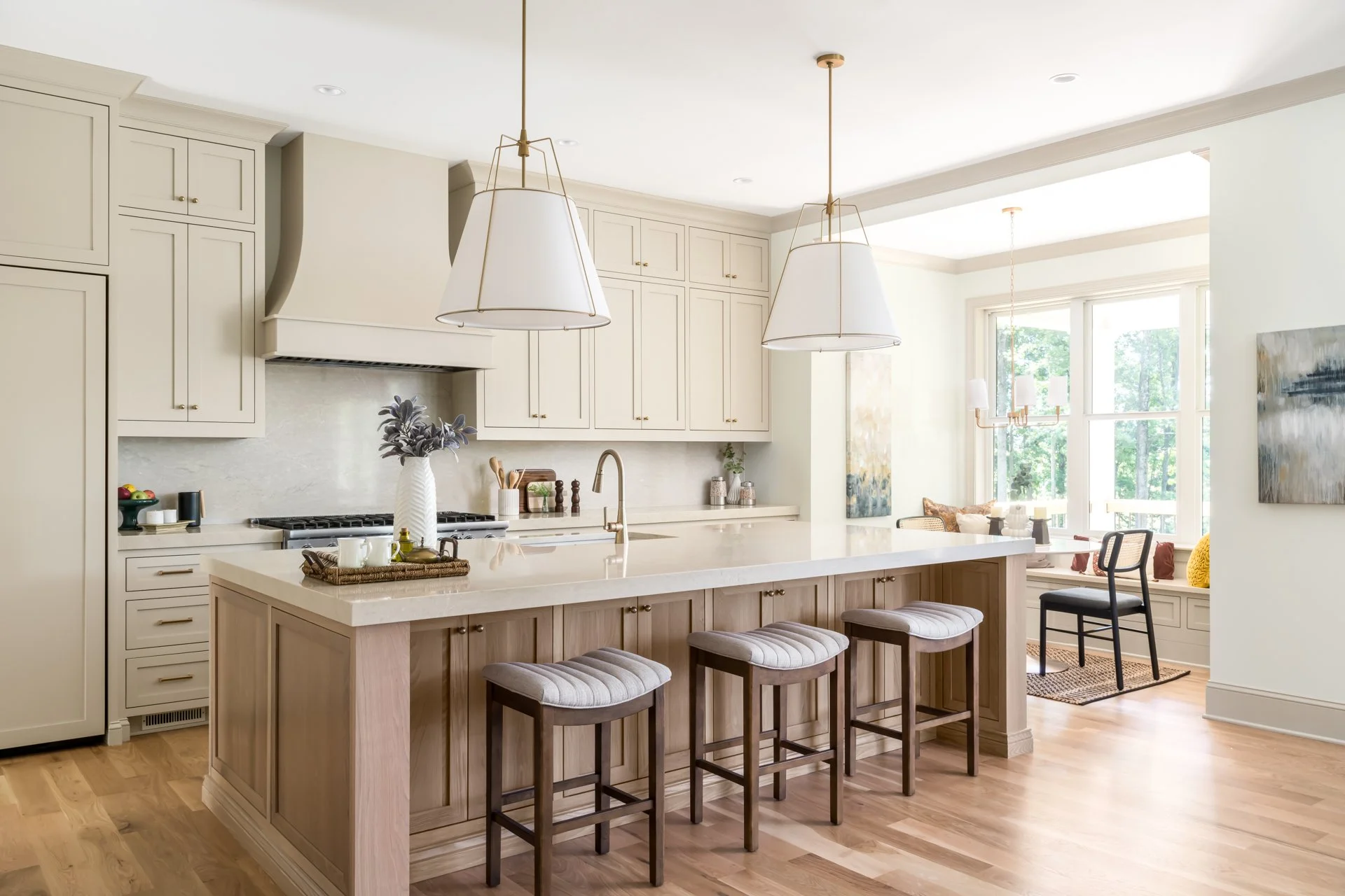 This elegant kitchen features floor-to-ceiling custom cabinetry in a warm neutral tone, a professional-grade gas range with custom hood, and an oversized quartz island perfect for entertaining. Brass fixtures, pendant lighting, and white oak wood flo