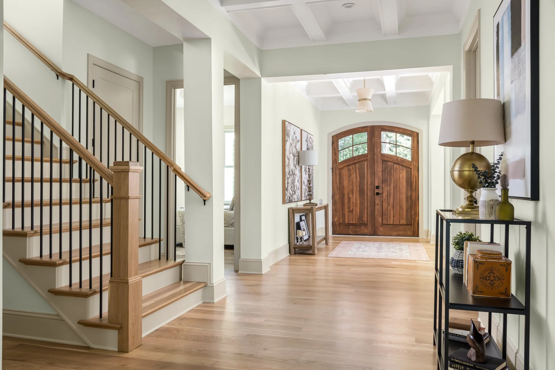 Step into a grand foyer that sets the tone for refined living. Featuring a handcrafted arched double wood door, coffered ceiling, and wide-plank hardwood flooring, the space is anchored by an open staircase with iron balusters and oak treads—blending