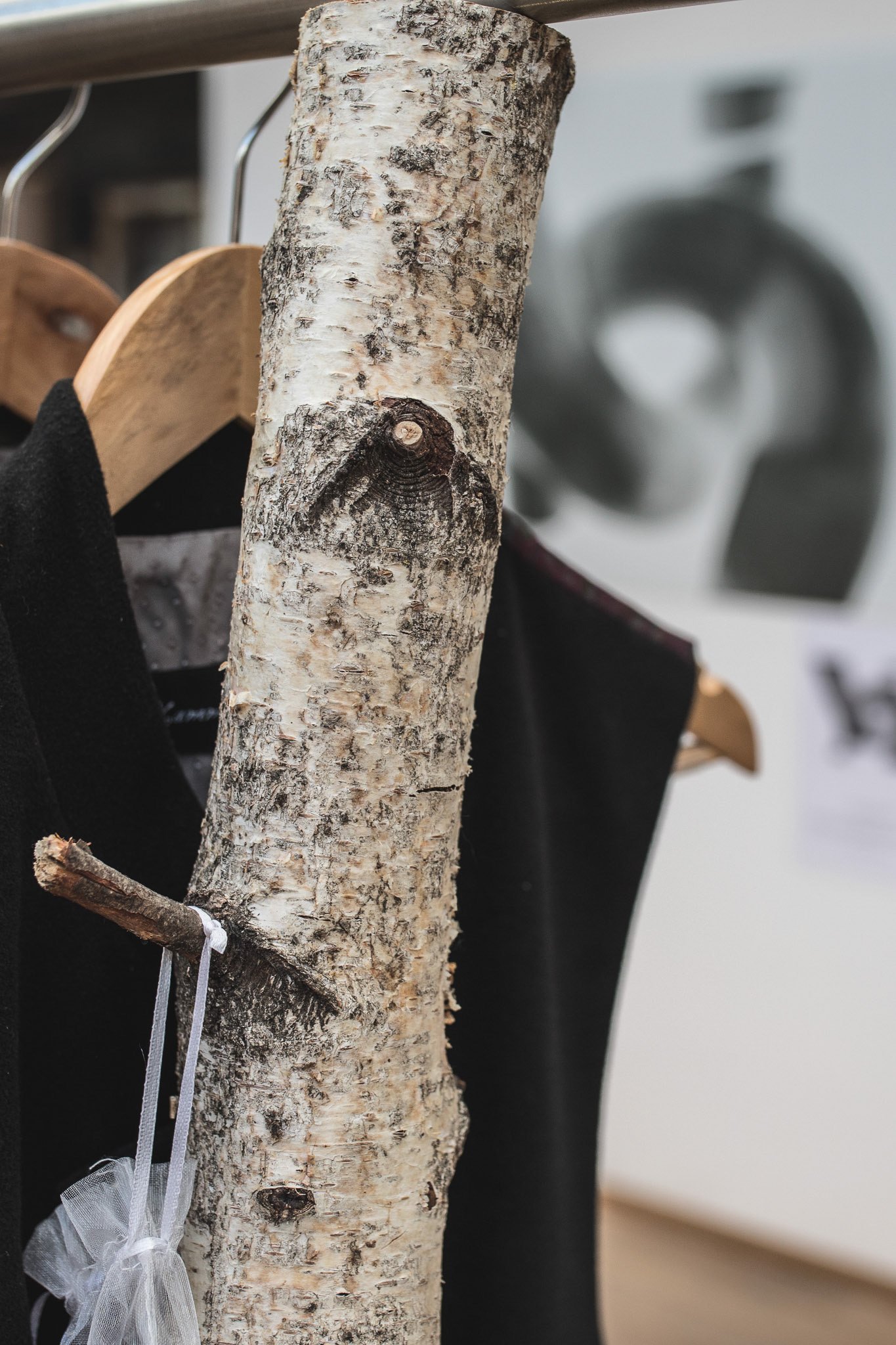 Ein Stück Birkenholz, das als Kleiderstange für hängende schwarze Kleidungsstücke dient, vermutlich in einem Ausstellungs- oder Verkaufsraum.