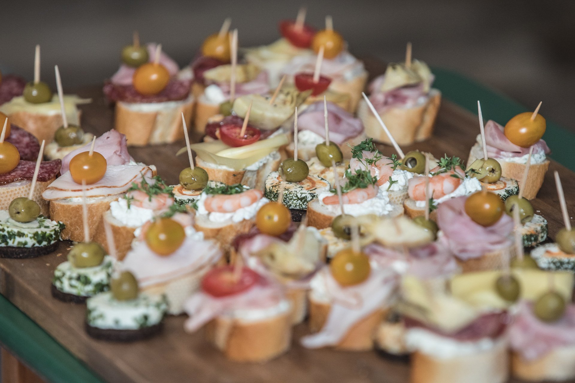 Verschiedene Canapés mit Brot, Garnelen, Schinken, Käse, Oliven und Tomaten auf einem Tablett arrangiert.