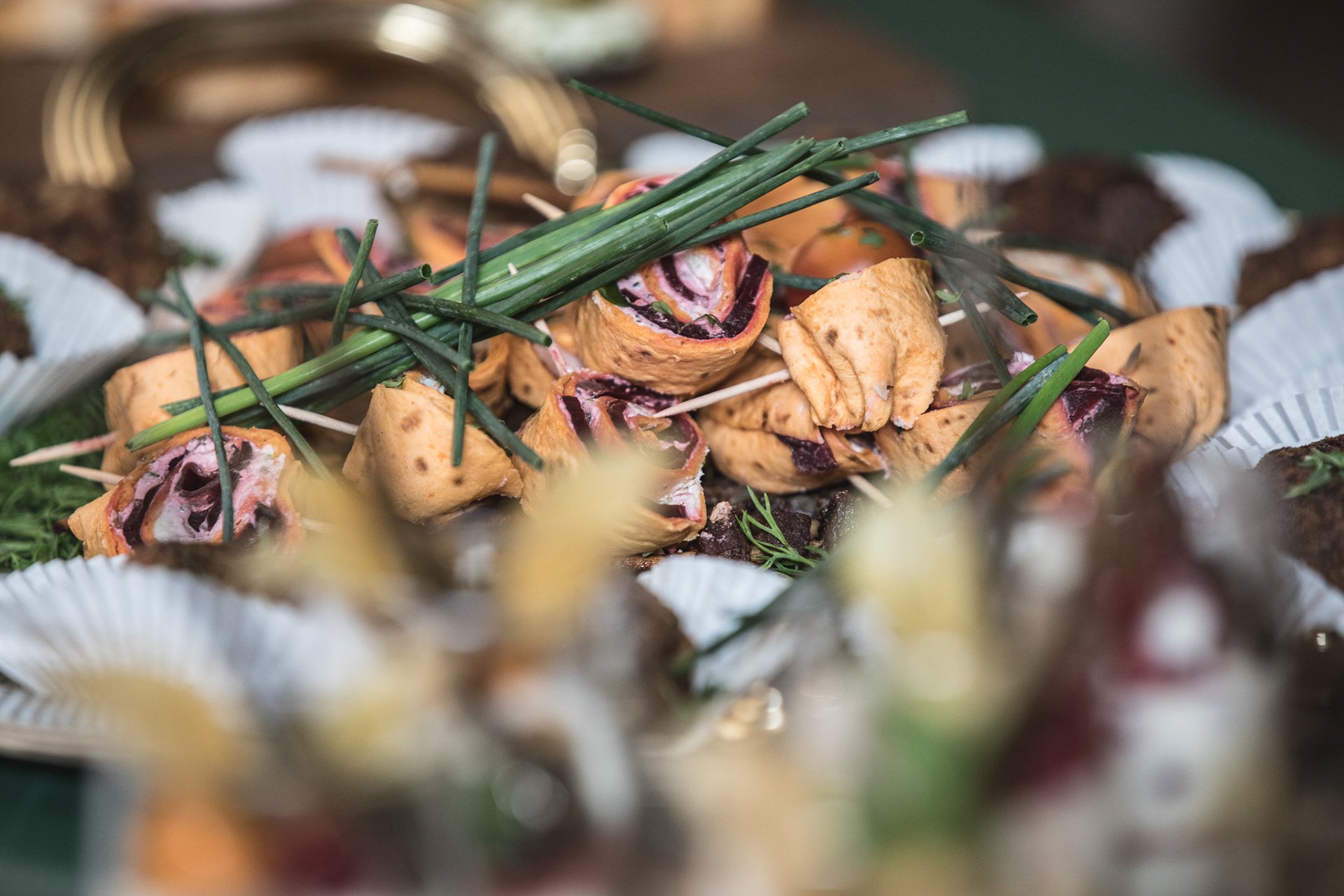 Buffet mit gerollten Sandwiches, gefüllt mit Aufschnitt und Gemüse, garniert mit Frühlingszwiebeln.