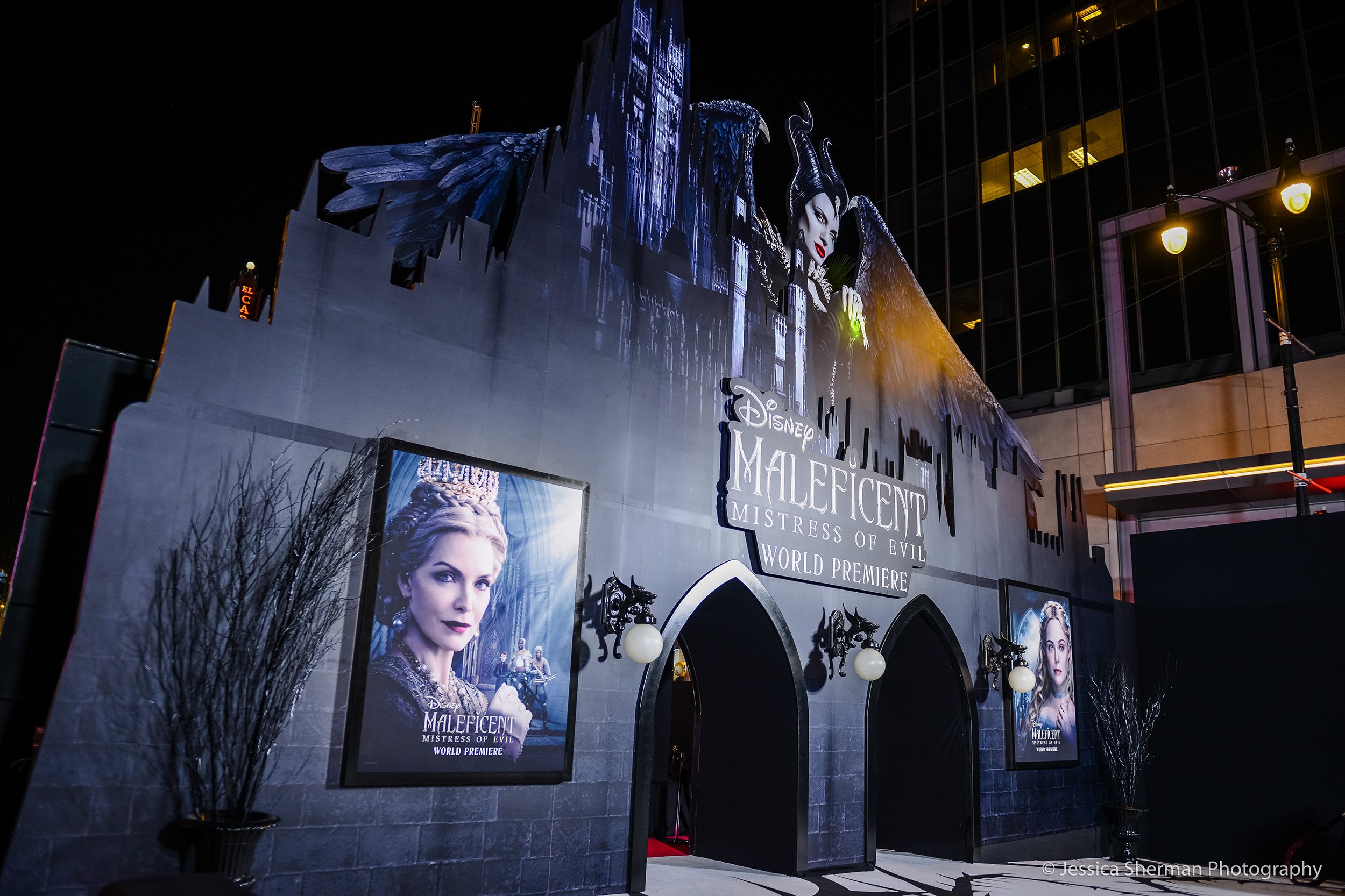 Nighttime premiere event for Disney's Maleficent: Mistress of Evil, with themed exterior decor resembling a castle, featuring large posters of the film and its villain Maleficent, with dark gothic architecture and lighting.