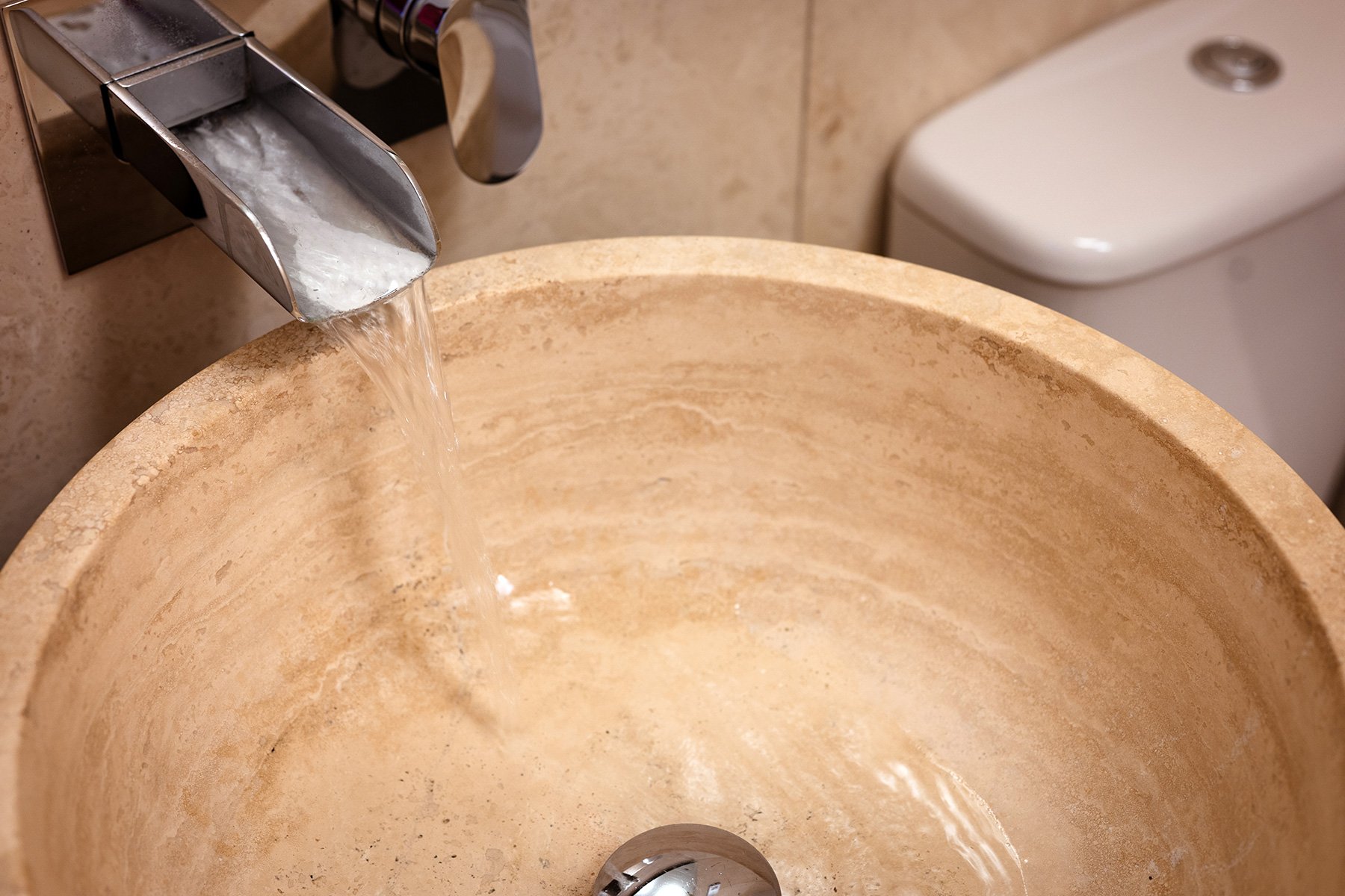 waterfall tap into cream coloured stoneware sink in a bathroom