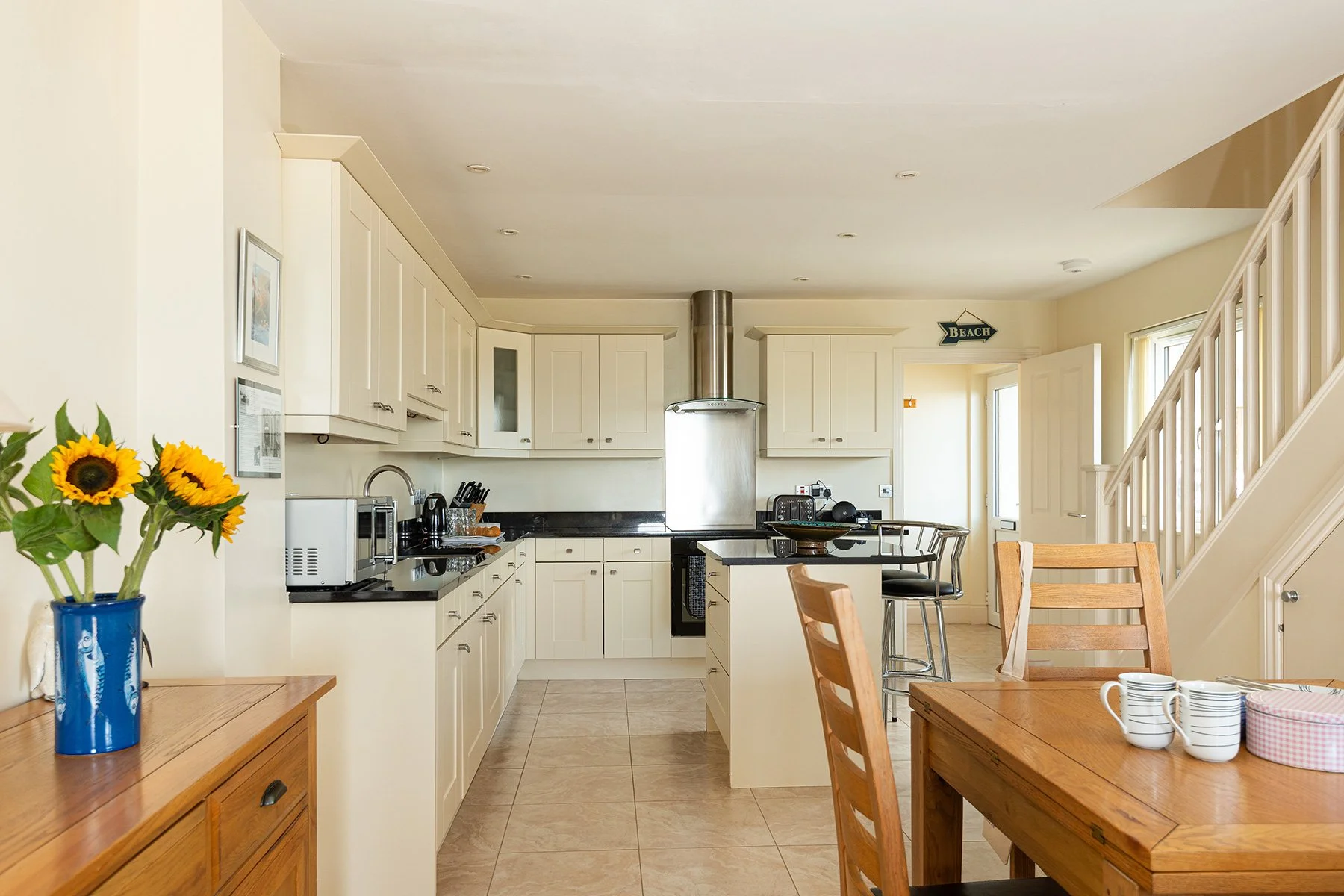 looking through the dining area at sea gems into the kitchen area with cream kitchen units and black worktops