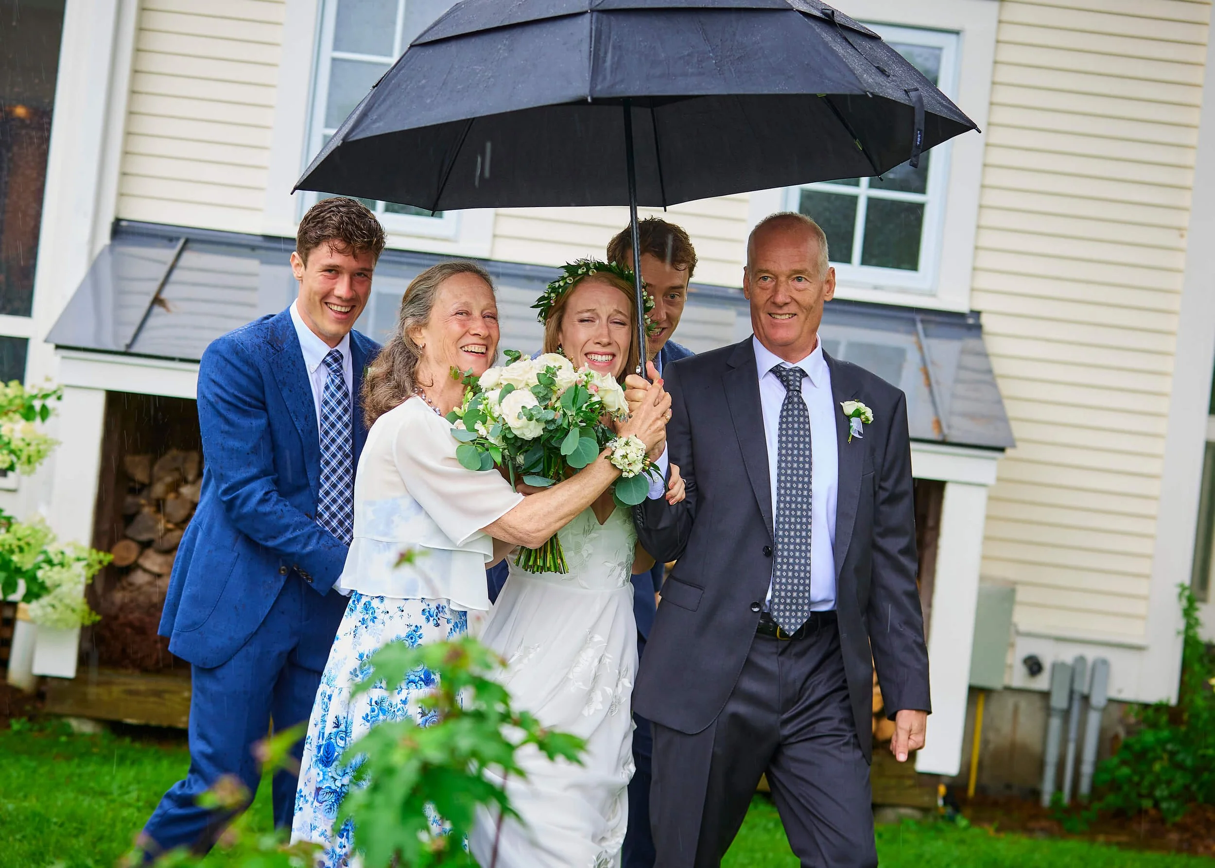A bride is escorted in the rain by her parents and brother to the tent for their wedding celebration.