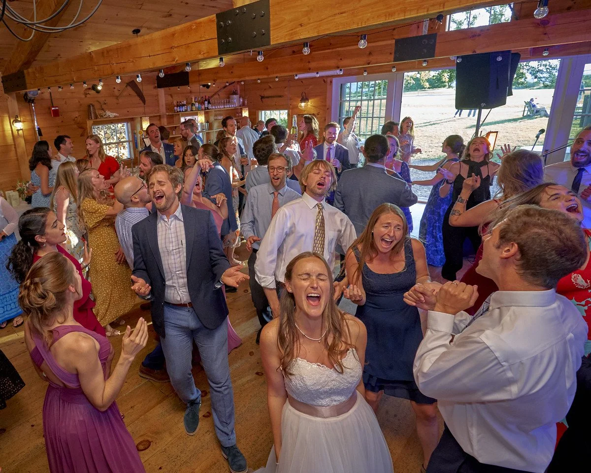 Photo of bride, groom, and wedding guestsd singing at the top of their lungs during a wedding reception in a barn in Vermont. Photo taken by Yeager Anderson.