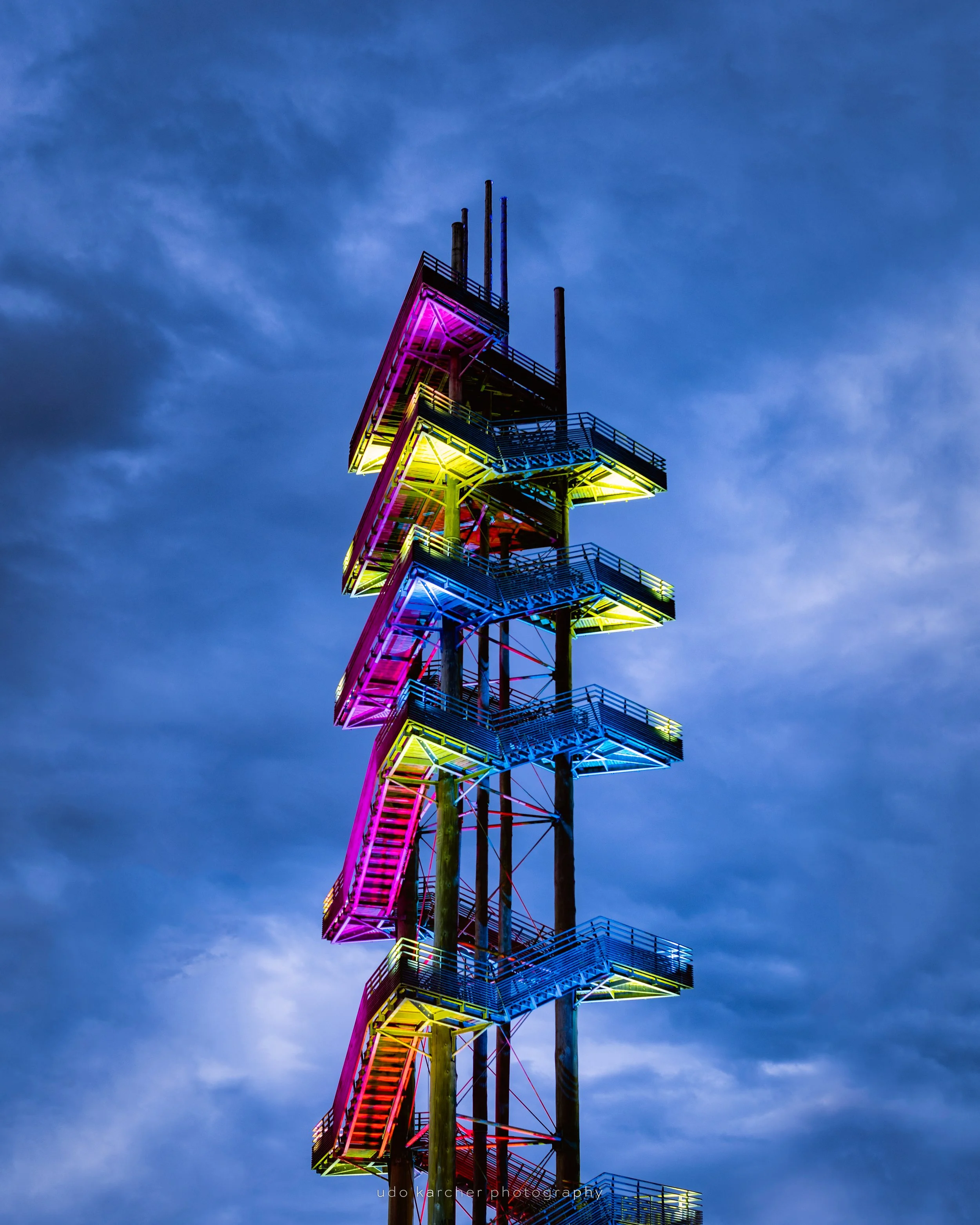 Illumination Under The Rain Clouds – Bunt angestrahlter Weißtannenturm vor Regenwolken in der Blauen Stunde