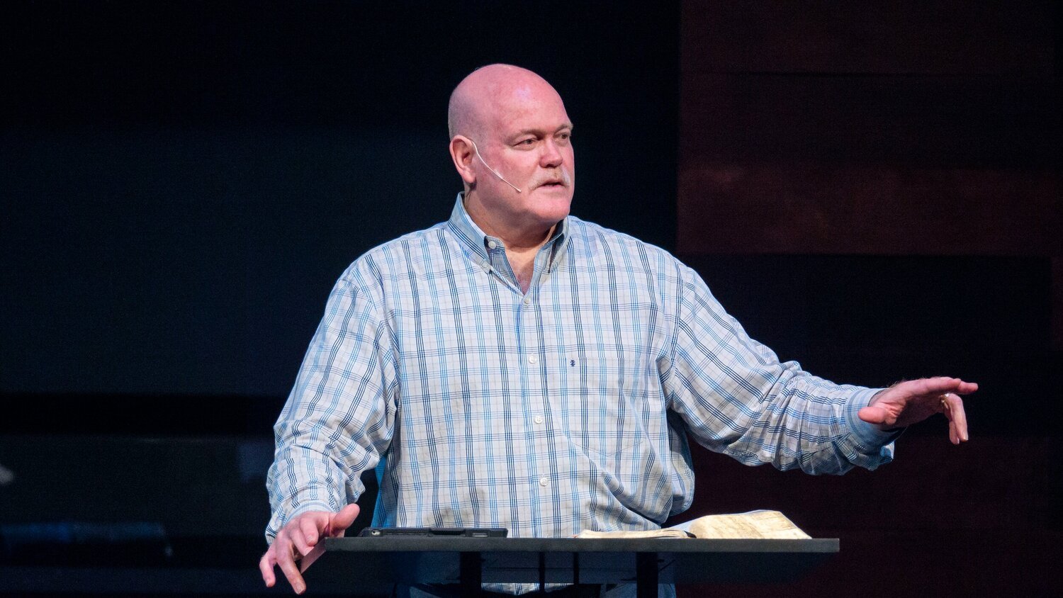 Man in plaid shirt speaking at a podium