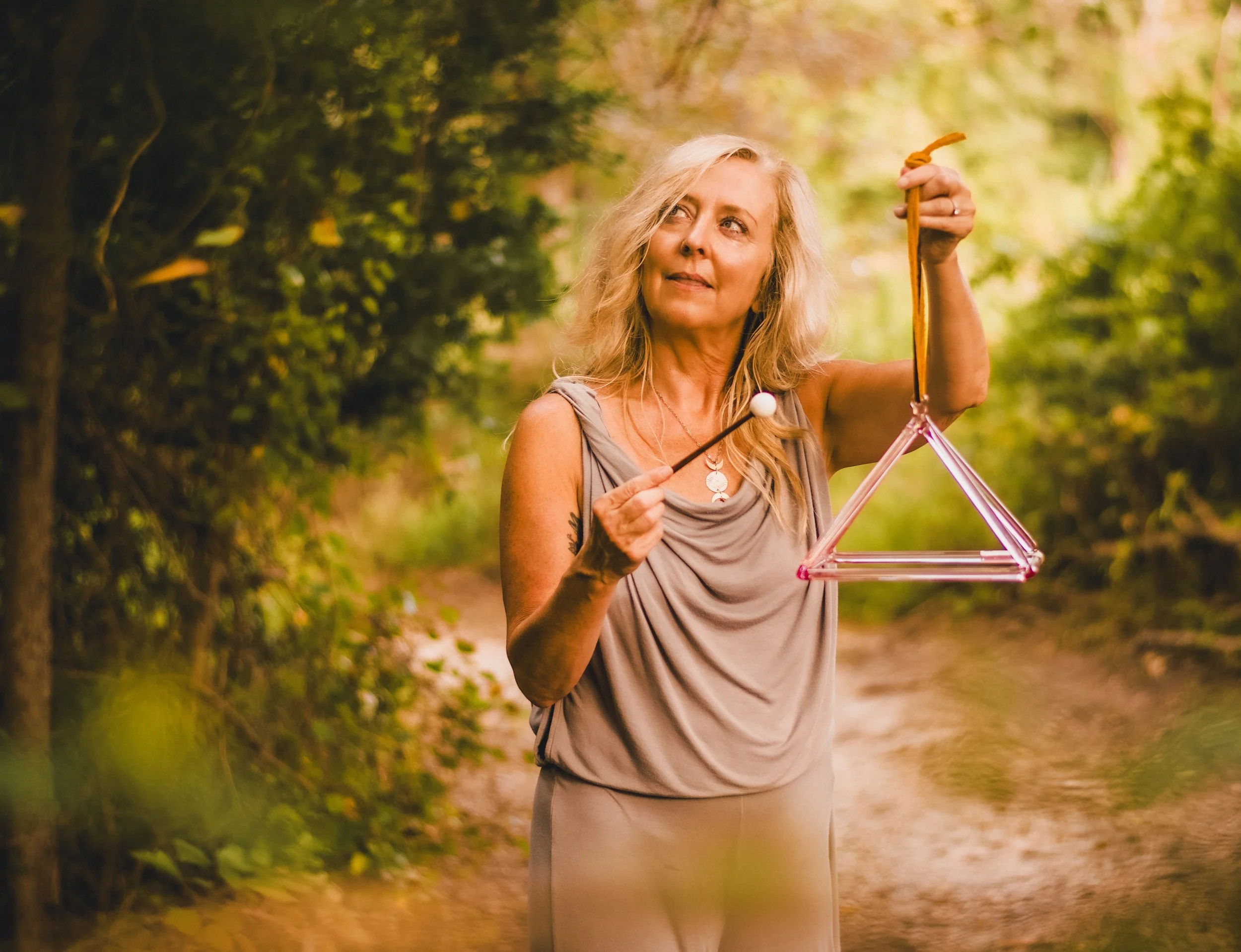A woman with blonde hair holding a triangle-shaped terrarium in a natural outdoor setting surrounded by greenery.