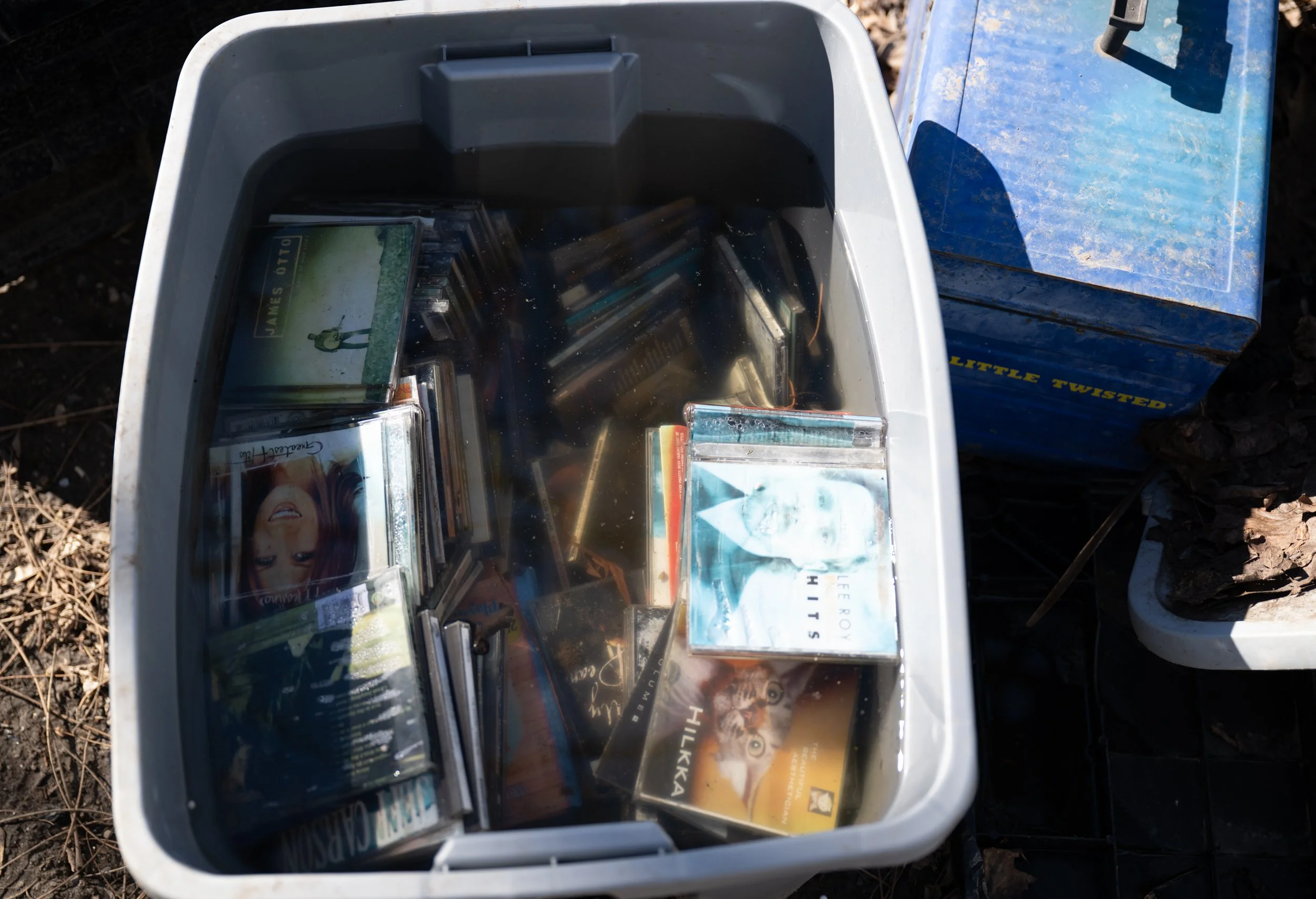 CD's sit in a water-filled bin at the campsite of Jenna and Dan Salamone on March 9, 2026. Salamone and her husband Dan then began living in tents on the property and are now looking to get housing. Her 14-year-old son currently lives with his biolog