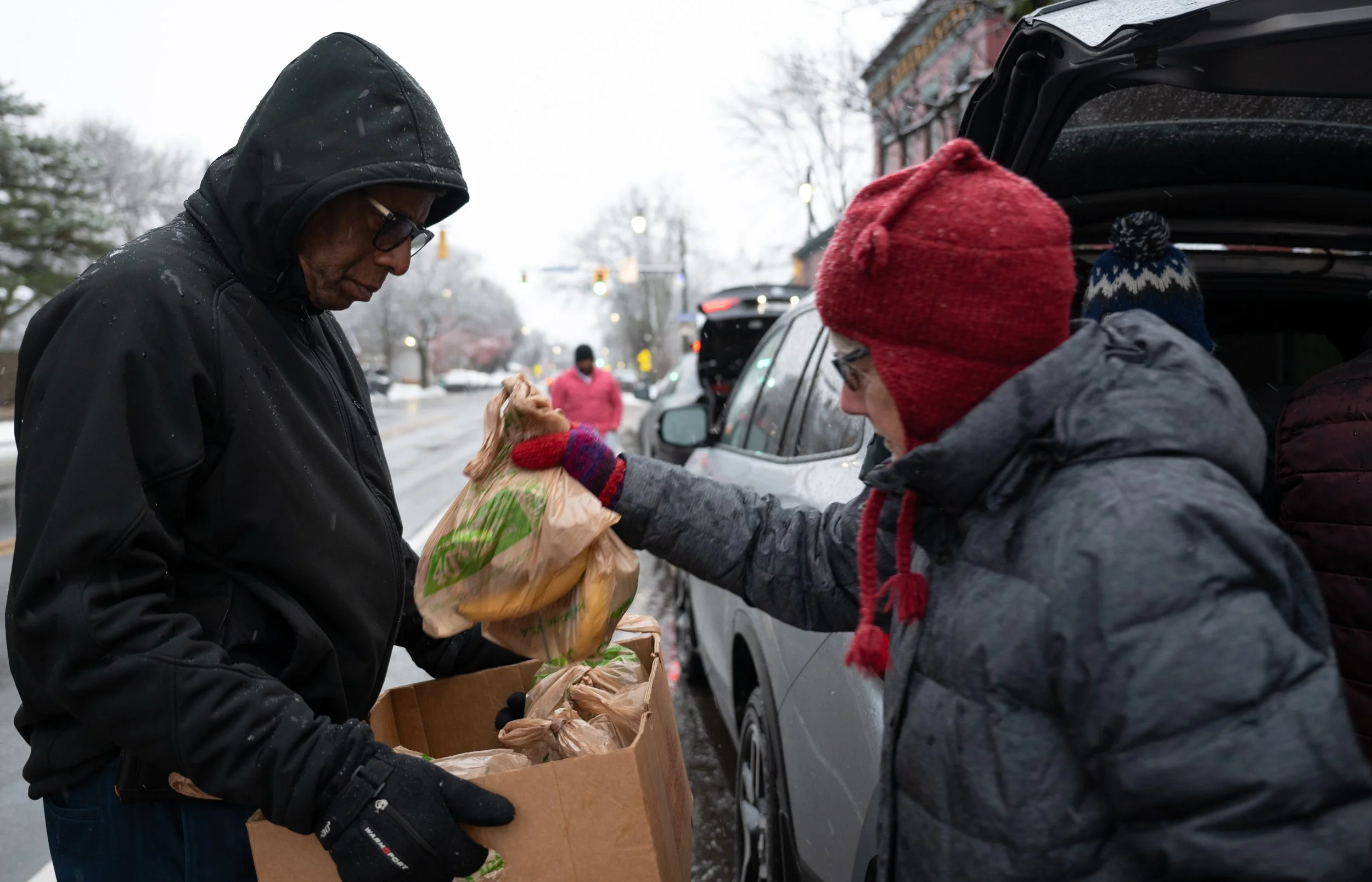 Calvin Barnes from PCHO, left, helps to carry prepared bags of food from a volunteer from the Blessed Sacrament Church, right, while doing street outreach on Dec. 23, 2025. 