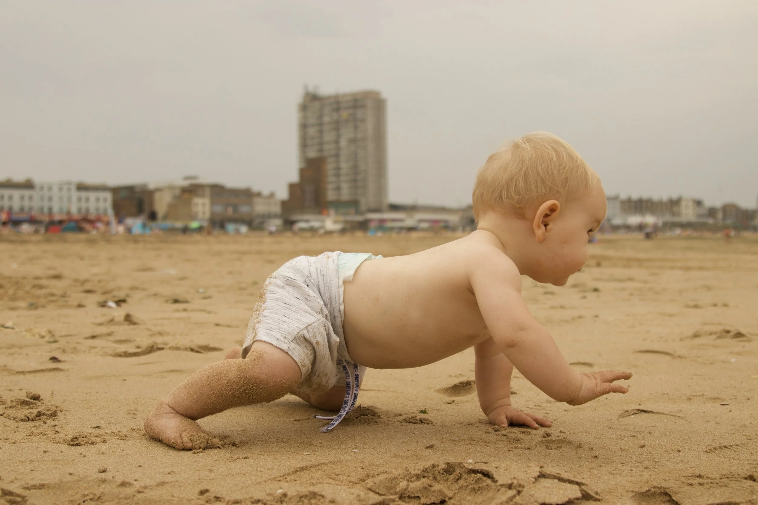 crawling child playing in the sand at the beach on holiday in the UK