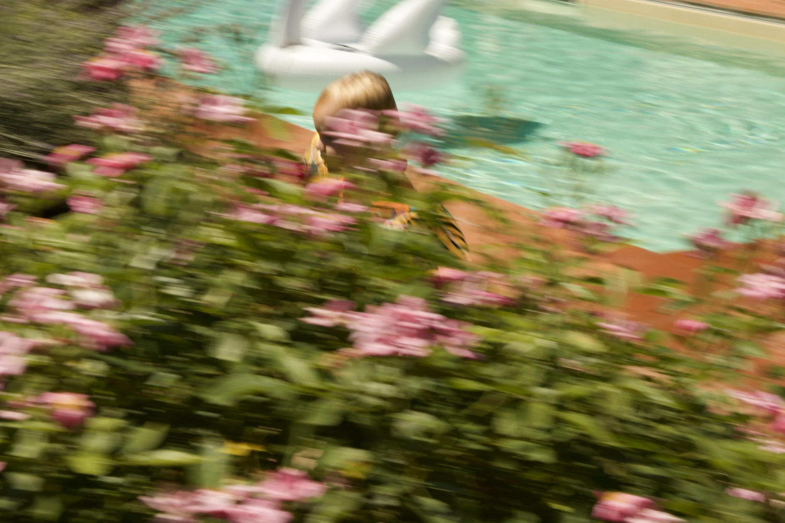 photograph of child playing by a flower-lined turquoise swimming pool