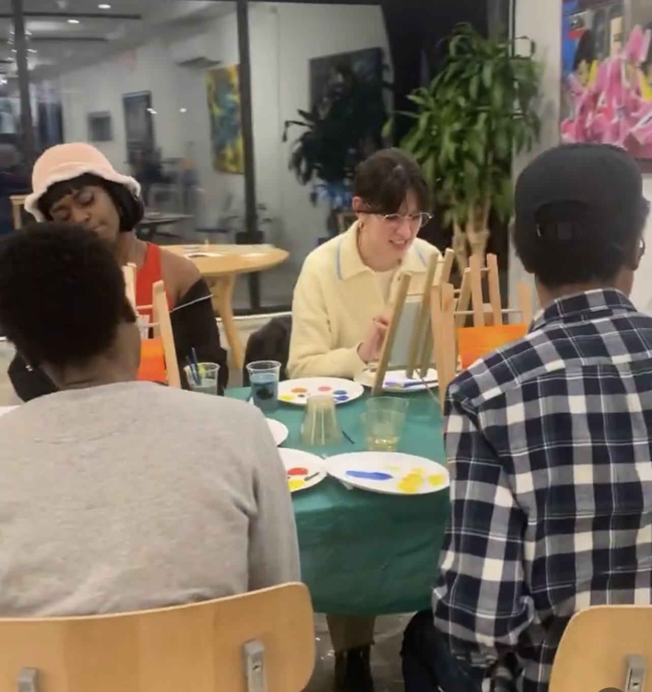 Group of young people painting at a table in a classroom or art studio.