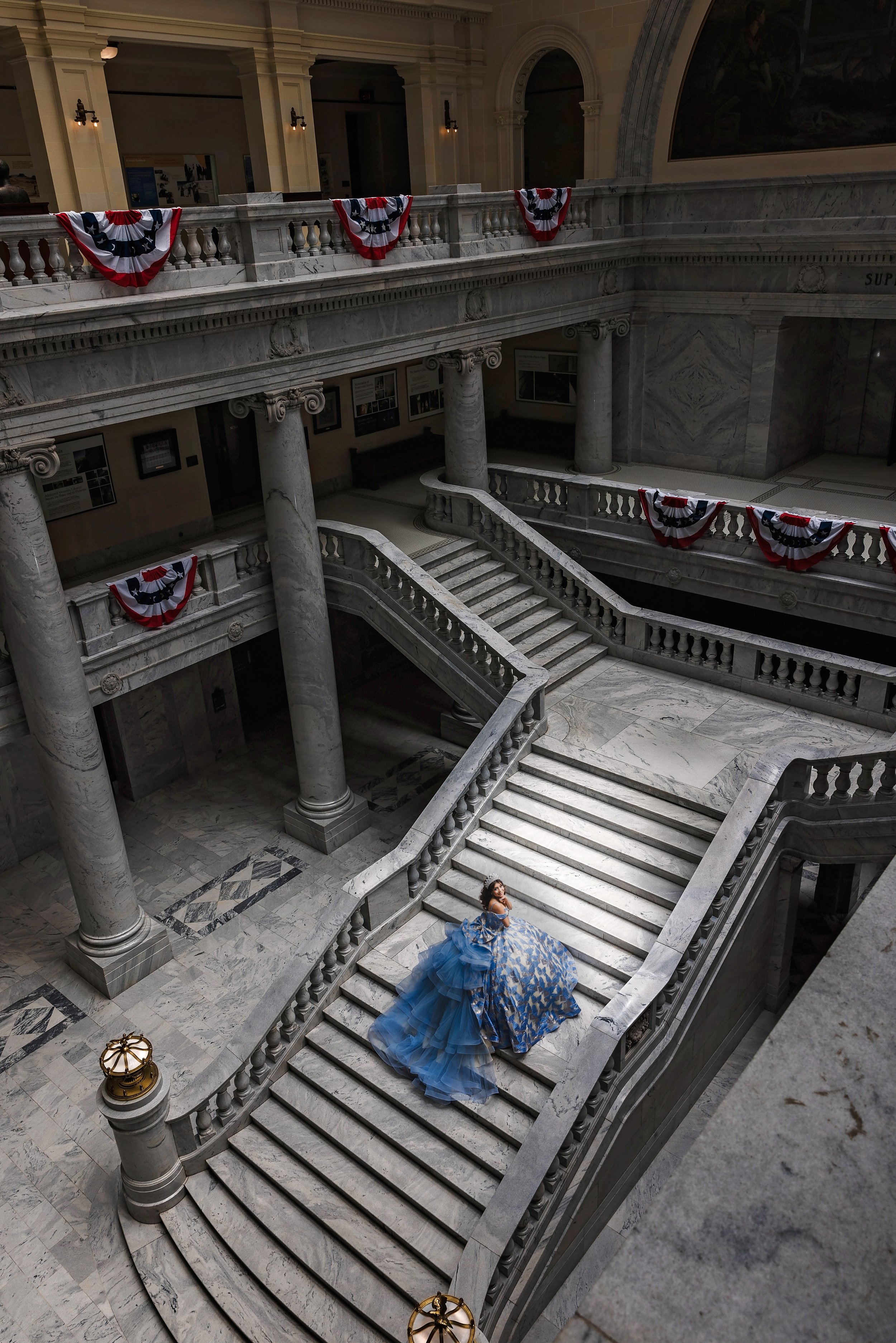 Create timeless memories with Once Upon a Quince, your go-to Quinceañera photography and videography expert in Utah. This dramatic portrait captures a Quinceañera elegantly posed on a grand staircase, her voluminous gown flowing down the steps in a b