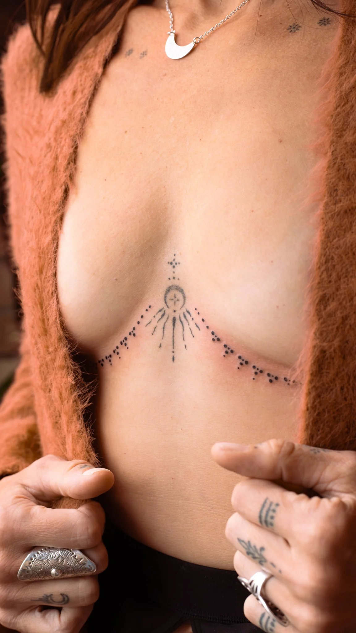 Minimal underboob tattoo by Toronto tattoo artist Alexandria Rising. Featuring fine dotwork and soft linework that flows like jewelry across the chest, this feminine, simple, and deeply ornamental design enhances the body’s natural curves.