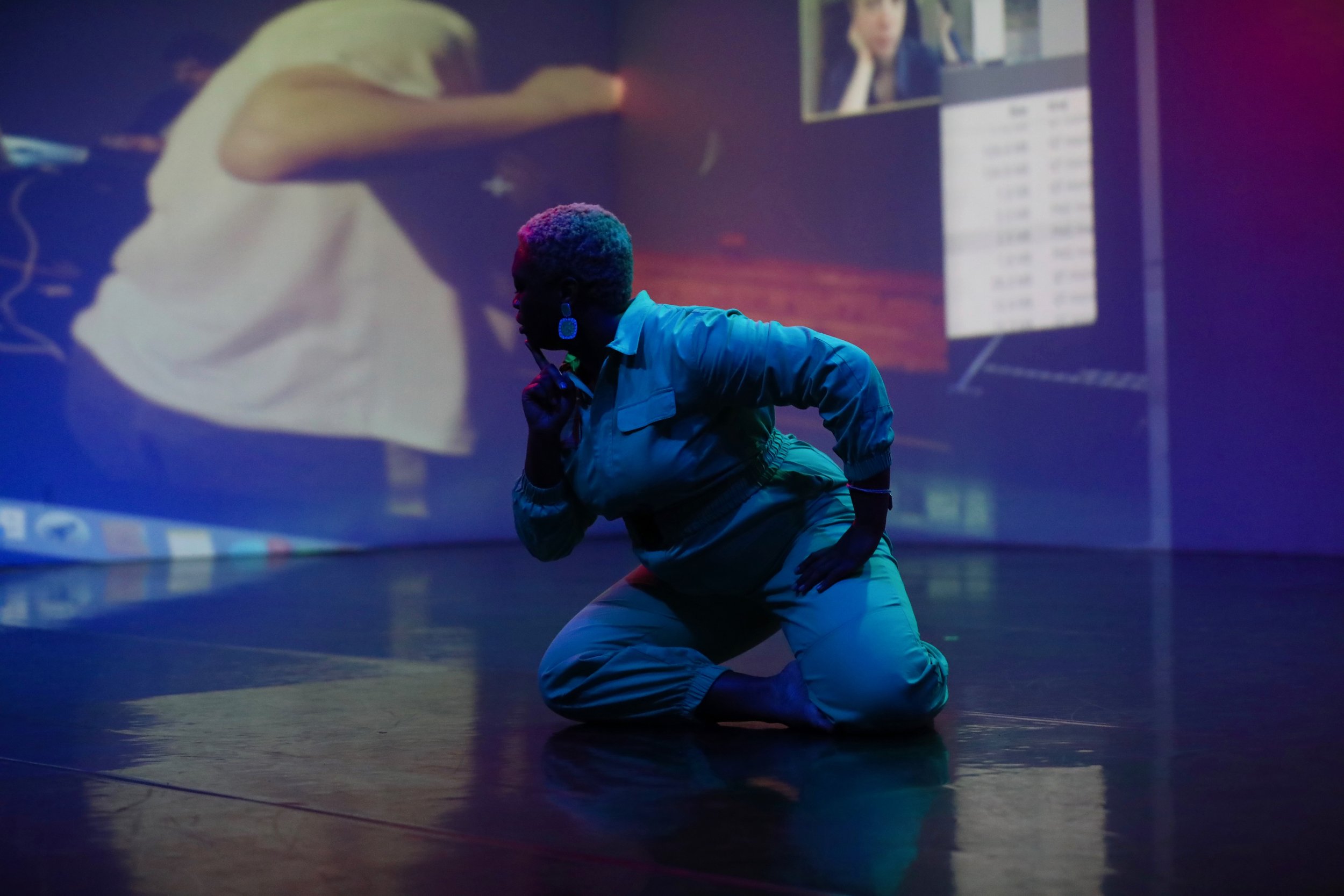 Ogemdi kneels on the ground and looks to one side.
