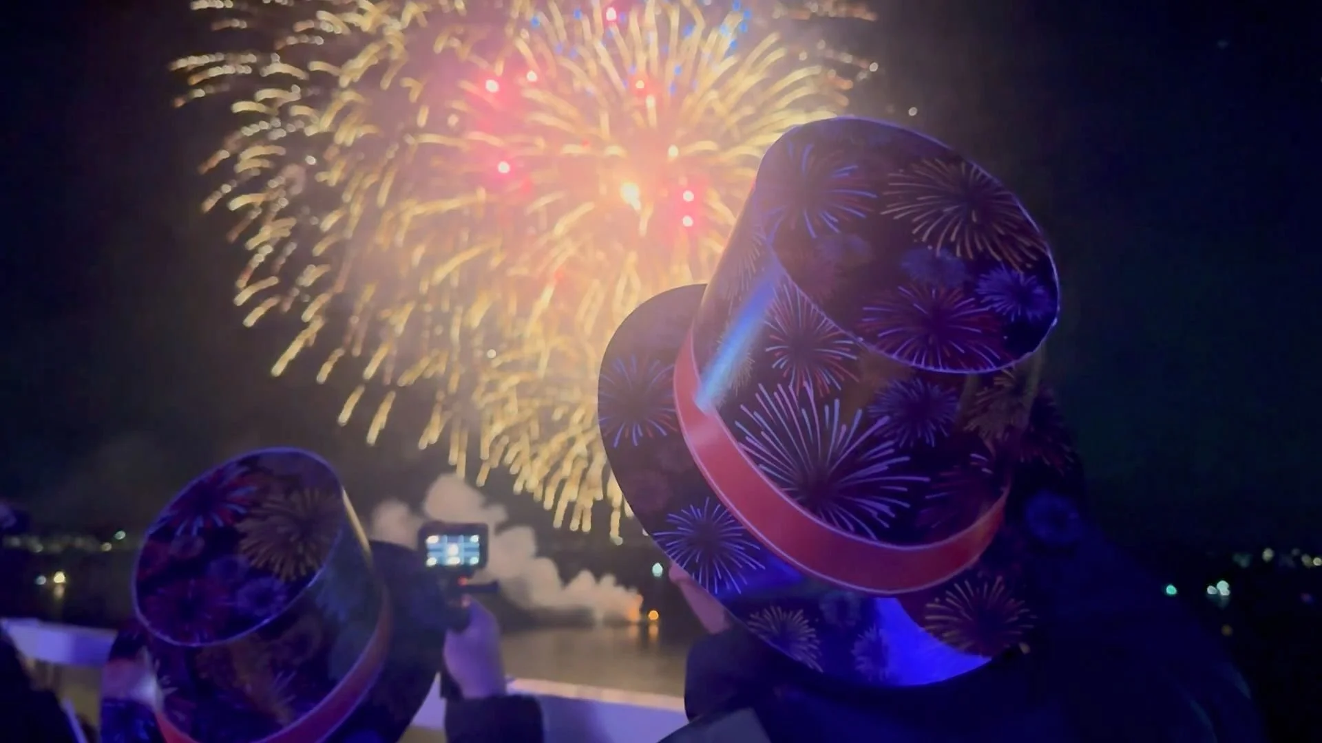 A couple wearing cardboard top hats watches New Year's Eve fireworks over Hobart.