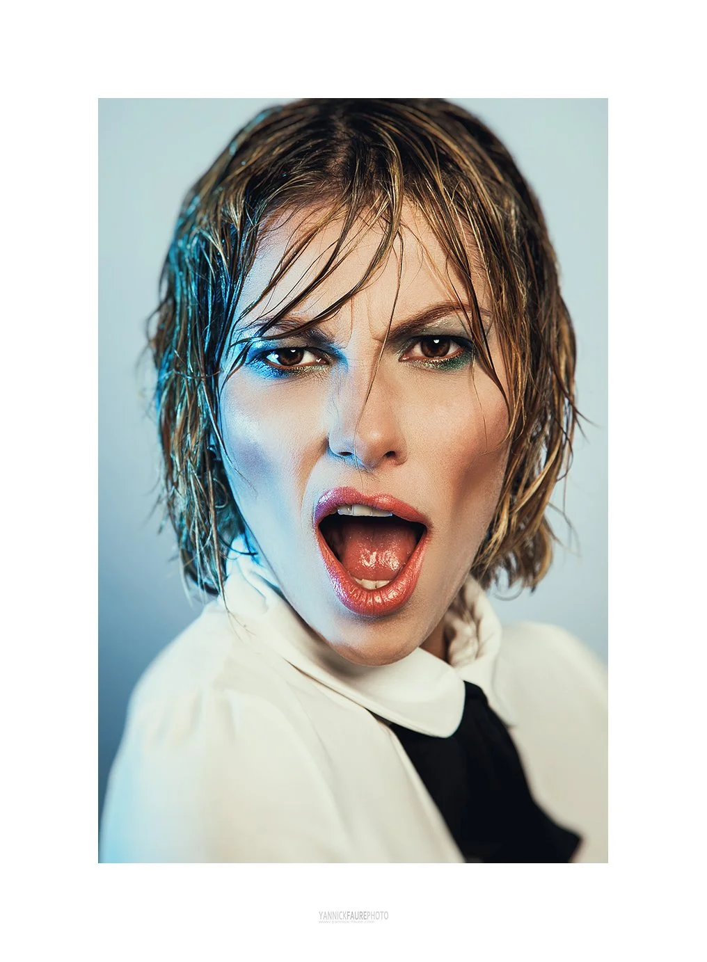 Une femme jeune avec des cheveux mouillés, portant un haut blanc à col noir, avec une expression faciale de surprise ou de choc, la bouche ouverte, image en gros plan.