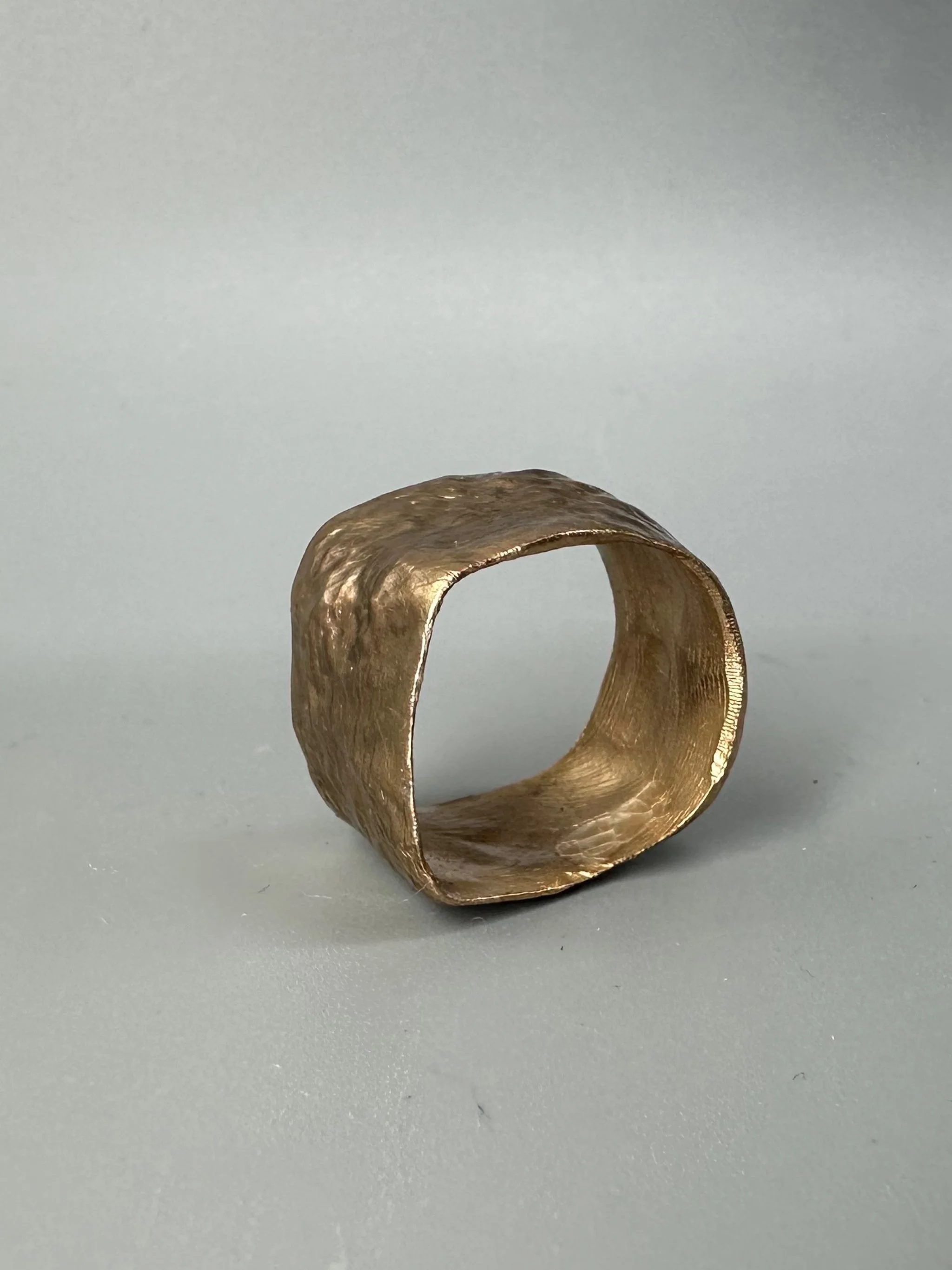Anello Fascia Longobarda di CōDICEDS in bronzo bocciardato, dalla forma ampia e irregolare.  Longobarda wide bronze ring by CōDICEDS, with a hammered surface and irregular shape.
