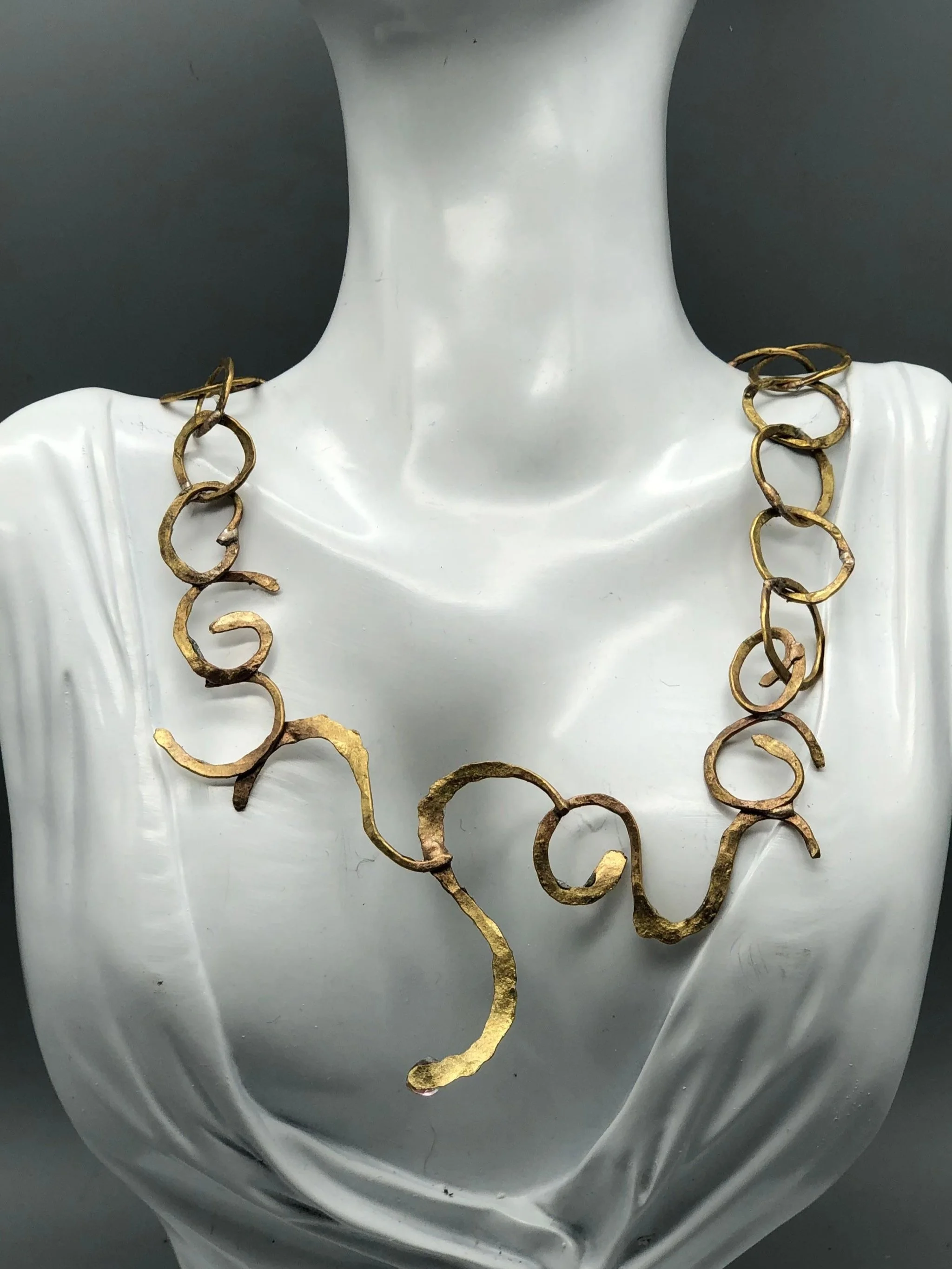 Collana Free Line di Claudia Cuzzeri in ottone opaco, con anelli irregolari e elemento centrale scultoreo a linea libera.