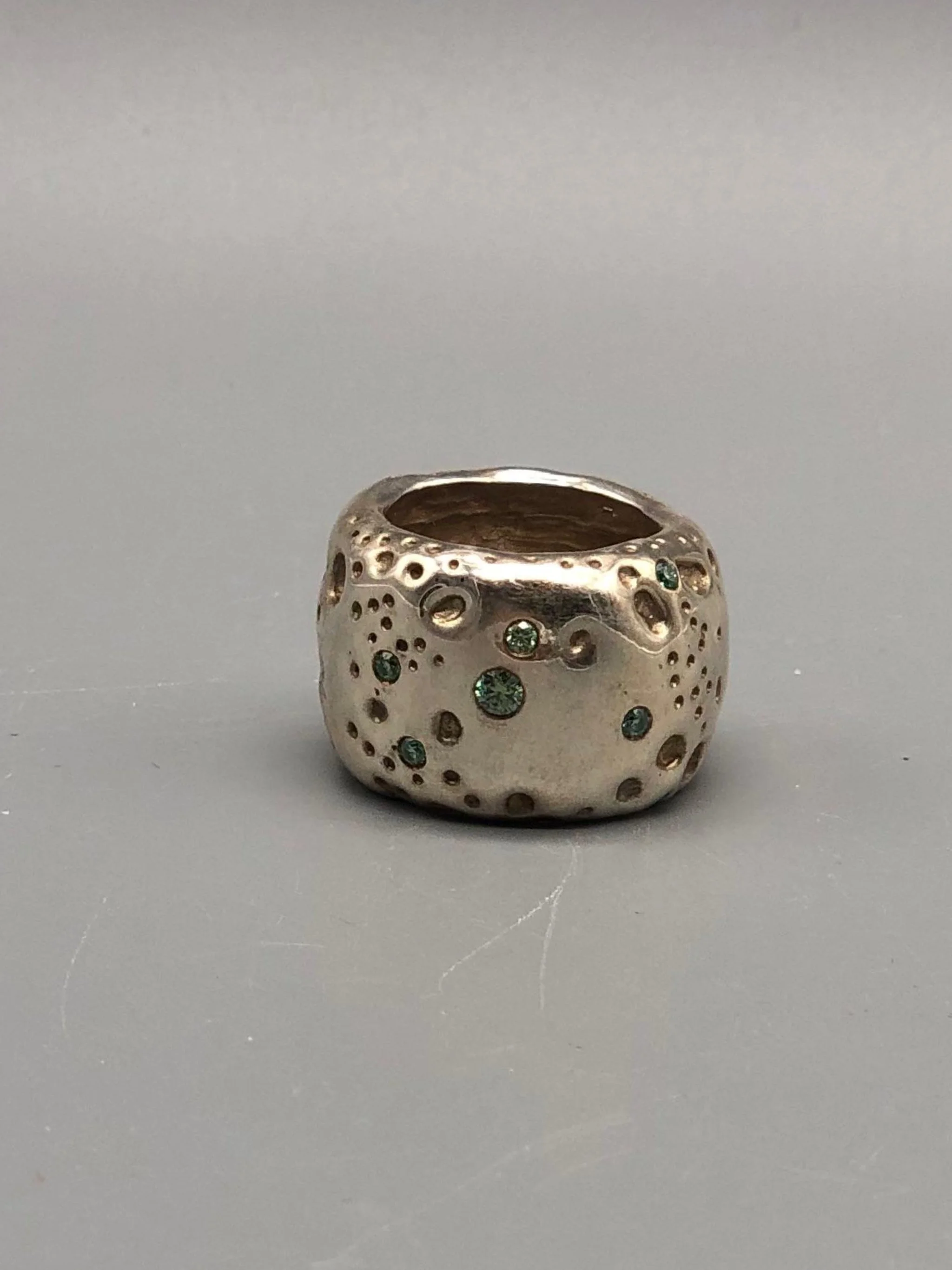Portas Luna ring with green moissanites, featuring an irregular cratered surface inspired by a lunar landscape.