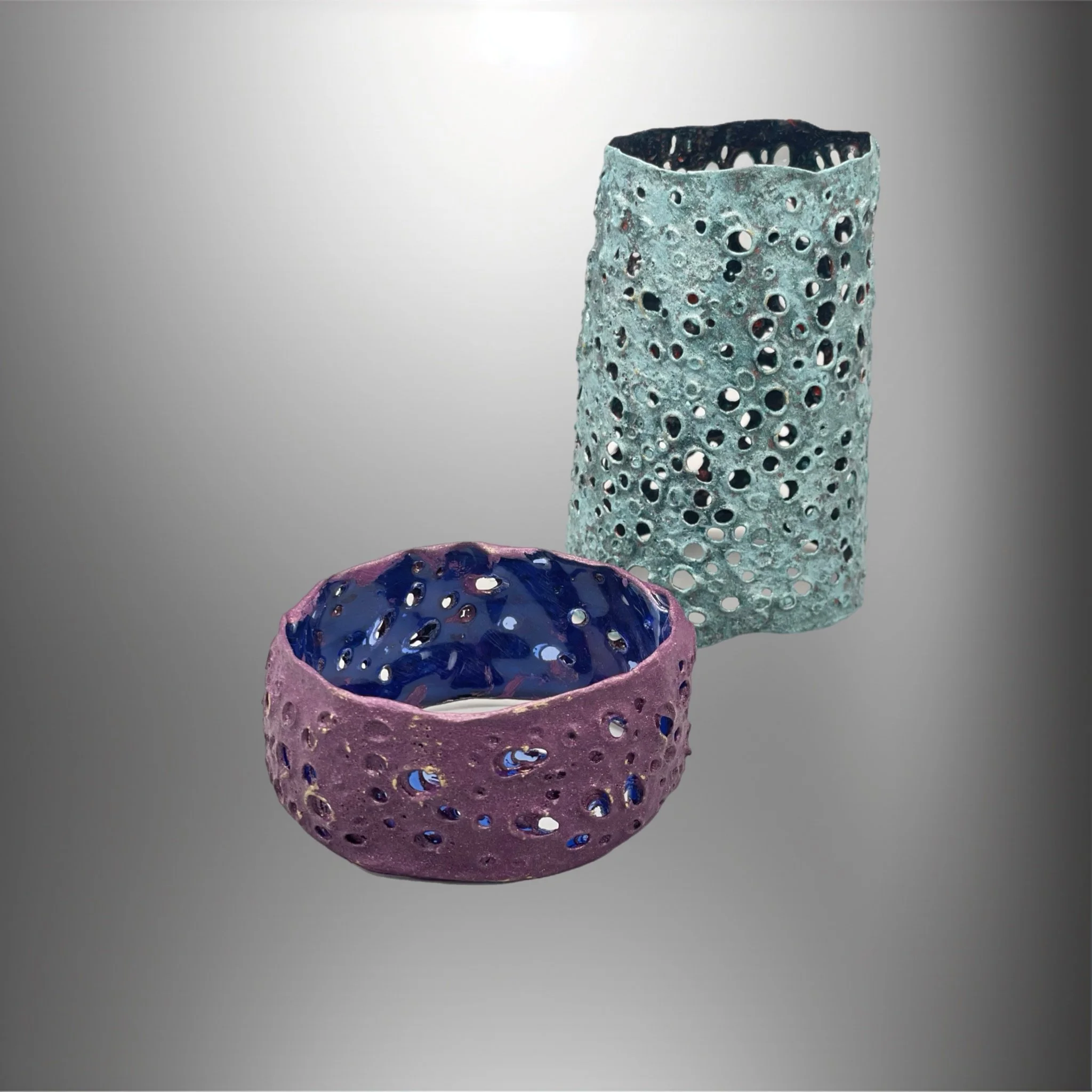 Due scatole di vetro perforate, una viola e una azzurra, su sfondo grigio
