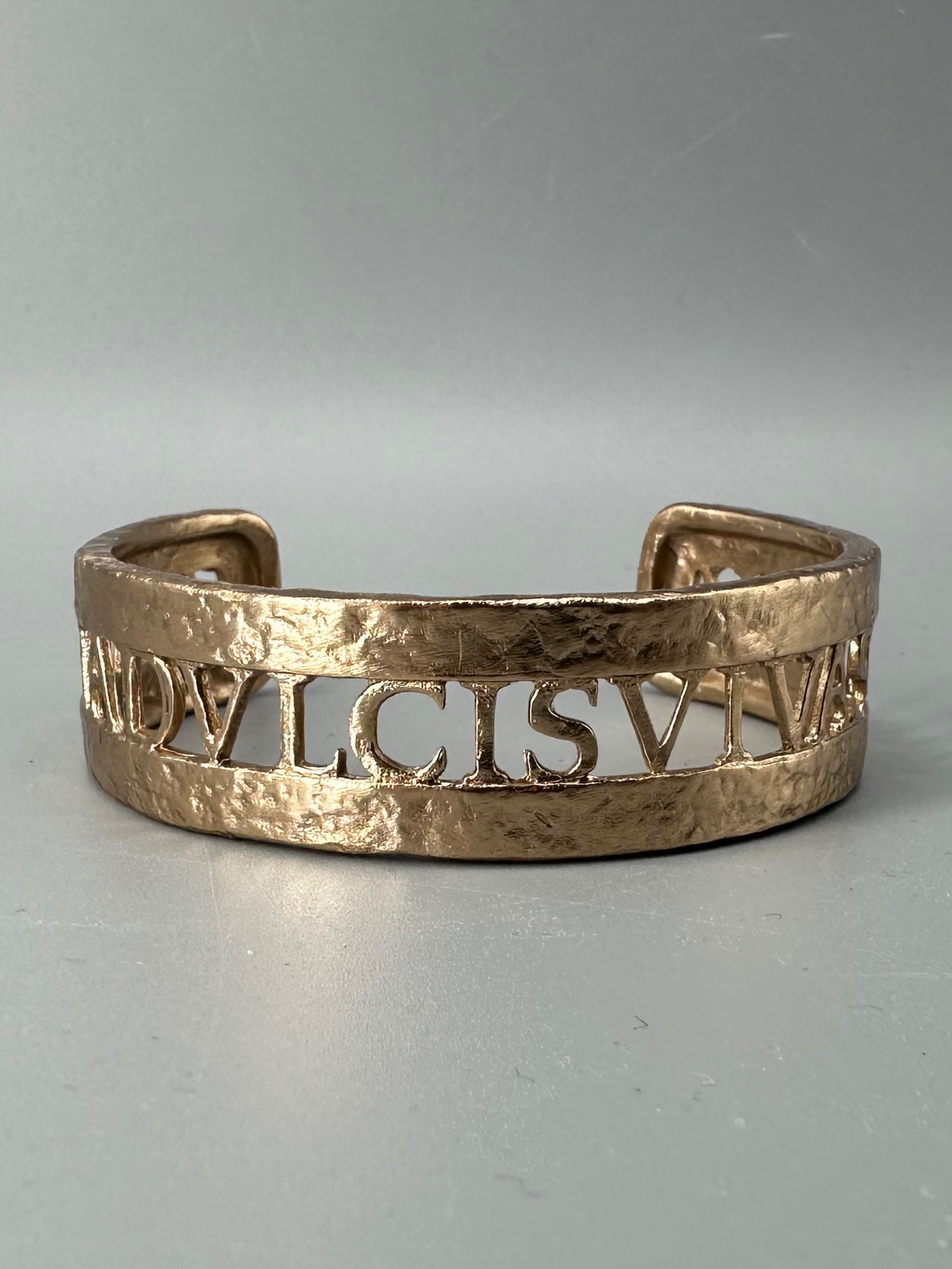 Bracciale Anima Dulcis di CōDICEDS in bronzo bocciardato, aperto e regolabile, con iscrizione latina traforata.  CōDICEDS Anima Dulcis open adjustable cuff in hammered bronze with openwork Latin inscr