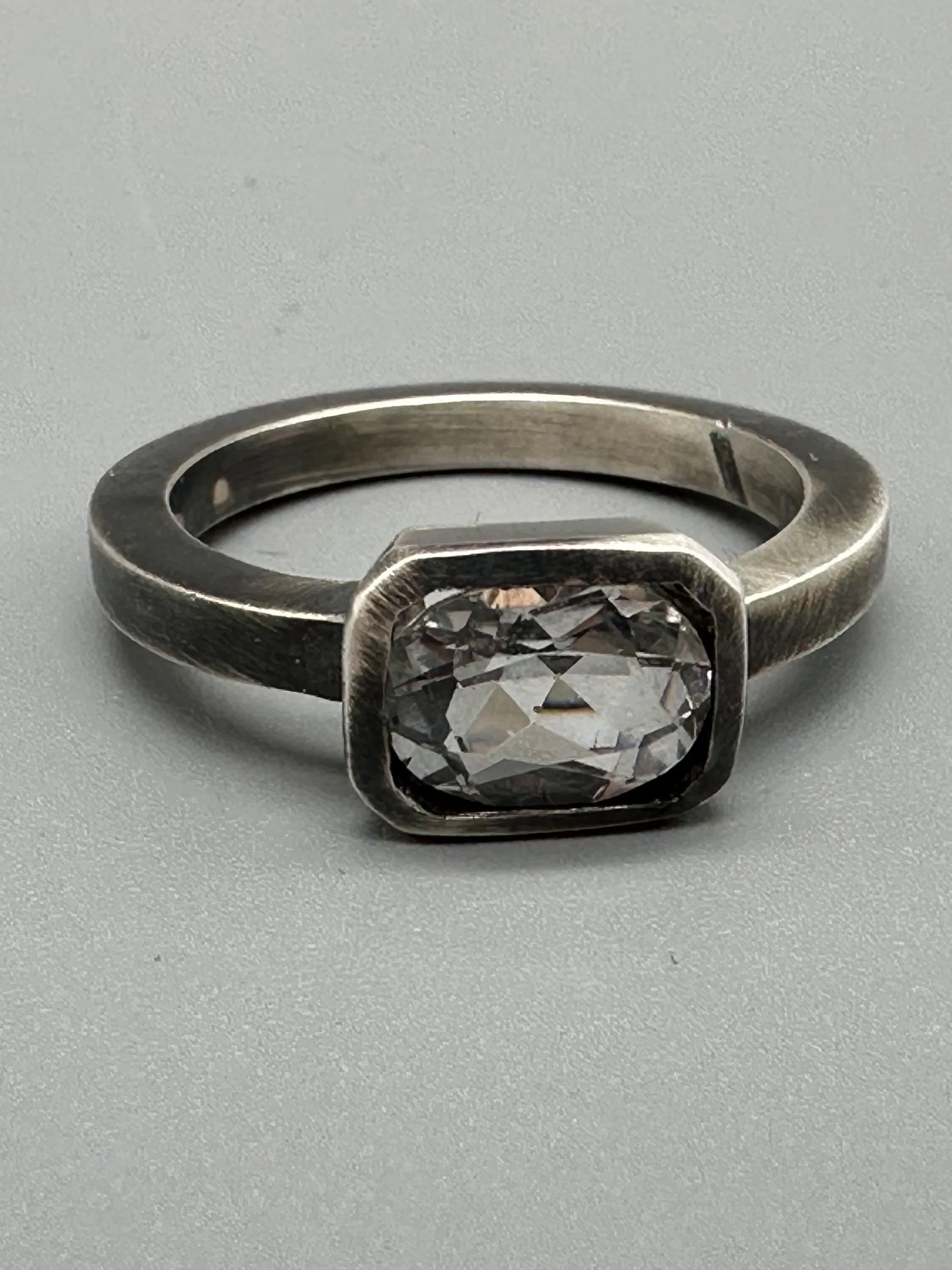 Anello White in Black in argento brunito con topazio bianco sfaccettato e castone geometrico. White in Black ring in oxidized sterling silver with faceted white topaz and geometric setting.