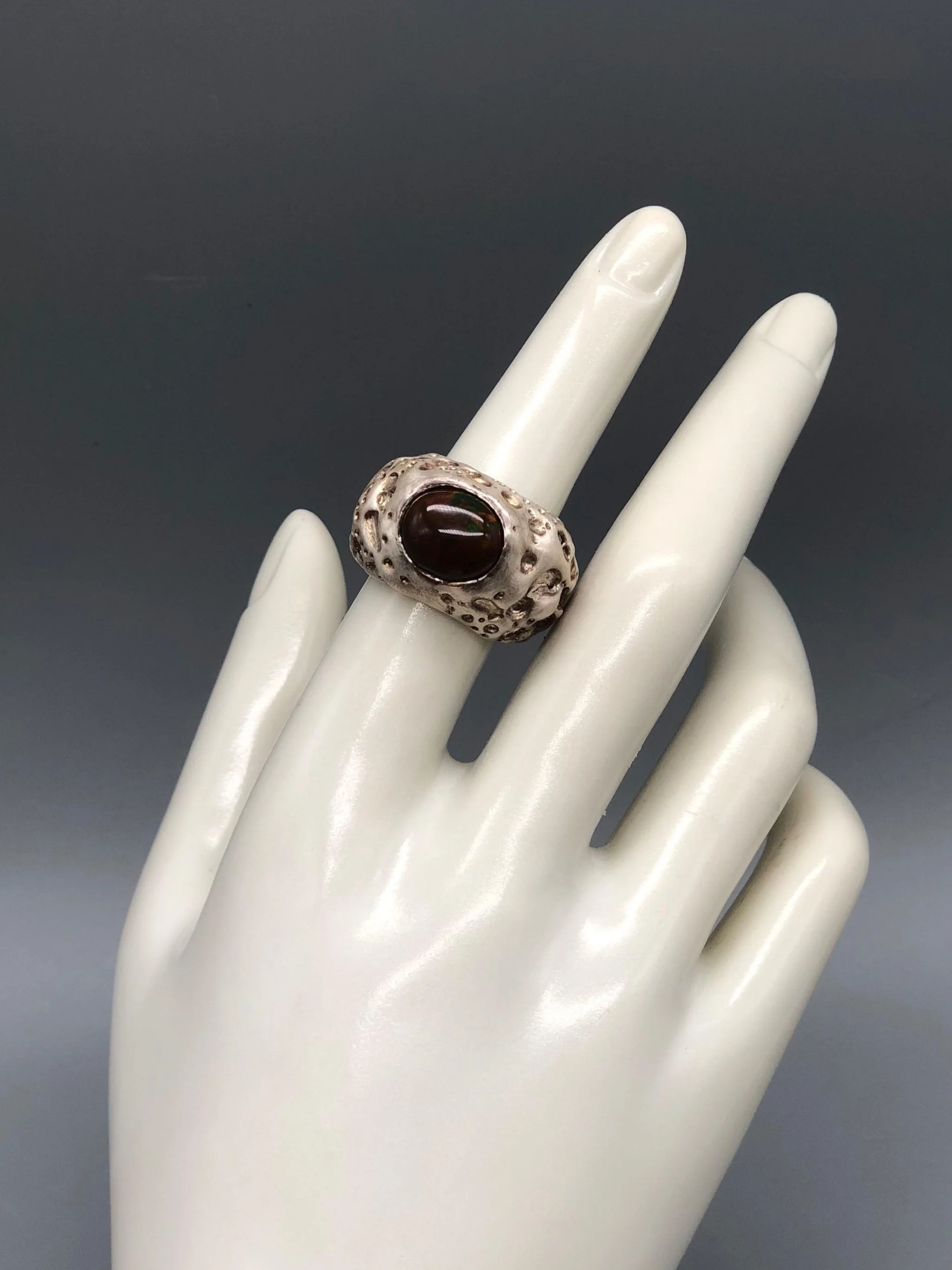 Luna ring by Portas Jewels in textured silver with a black opal showing deep red and green reflections.