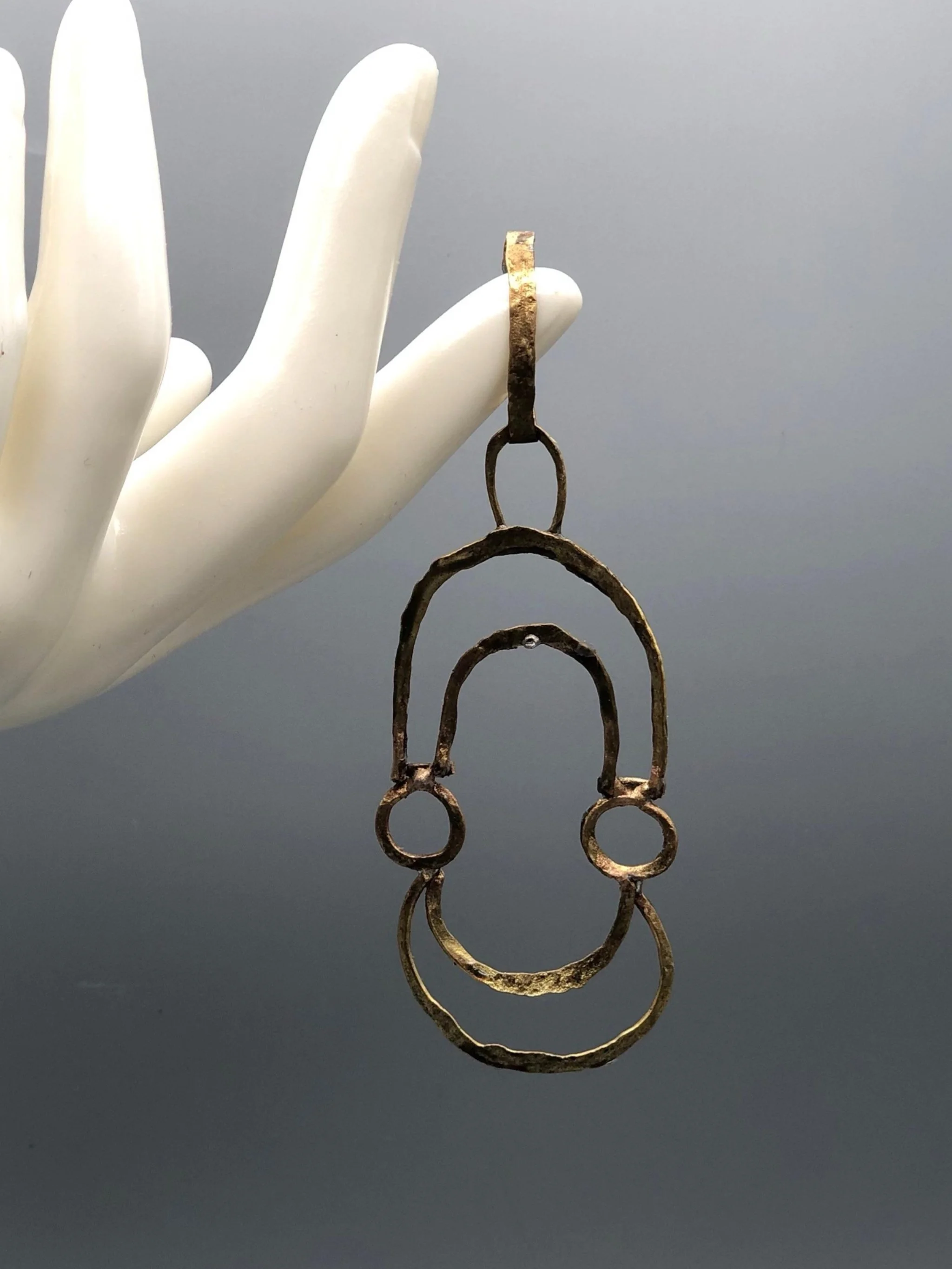 Ciondolo Contour di Claudia Cuzzeri in ottone opaco, con profili irregolari concentrici e forma aperta.