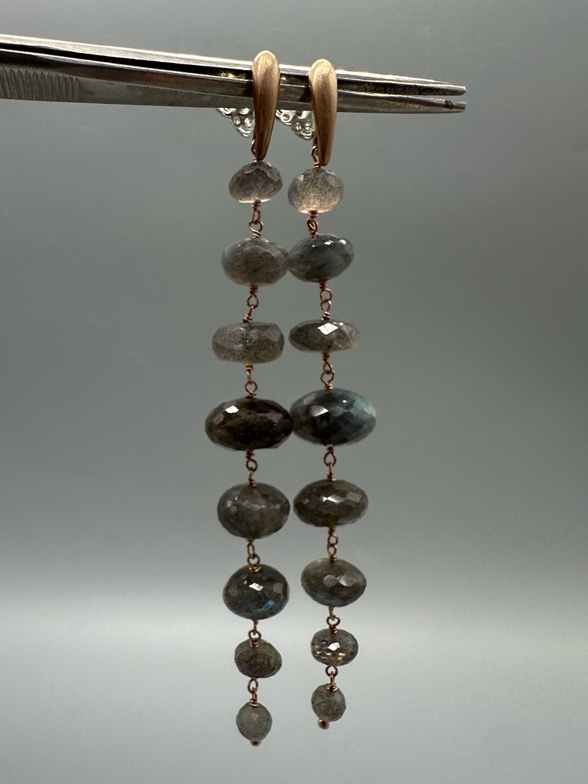 Orecchini Bold Labradorite con pietre grigie sfaccettate dai riflessi blu e verdi, disposte in verticale. Bold Labradorite earrings with vertically arranged faceted grey gemstones and blue-green refle